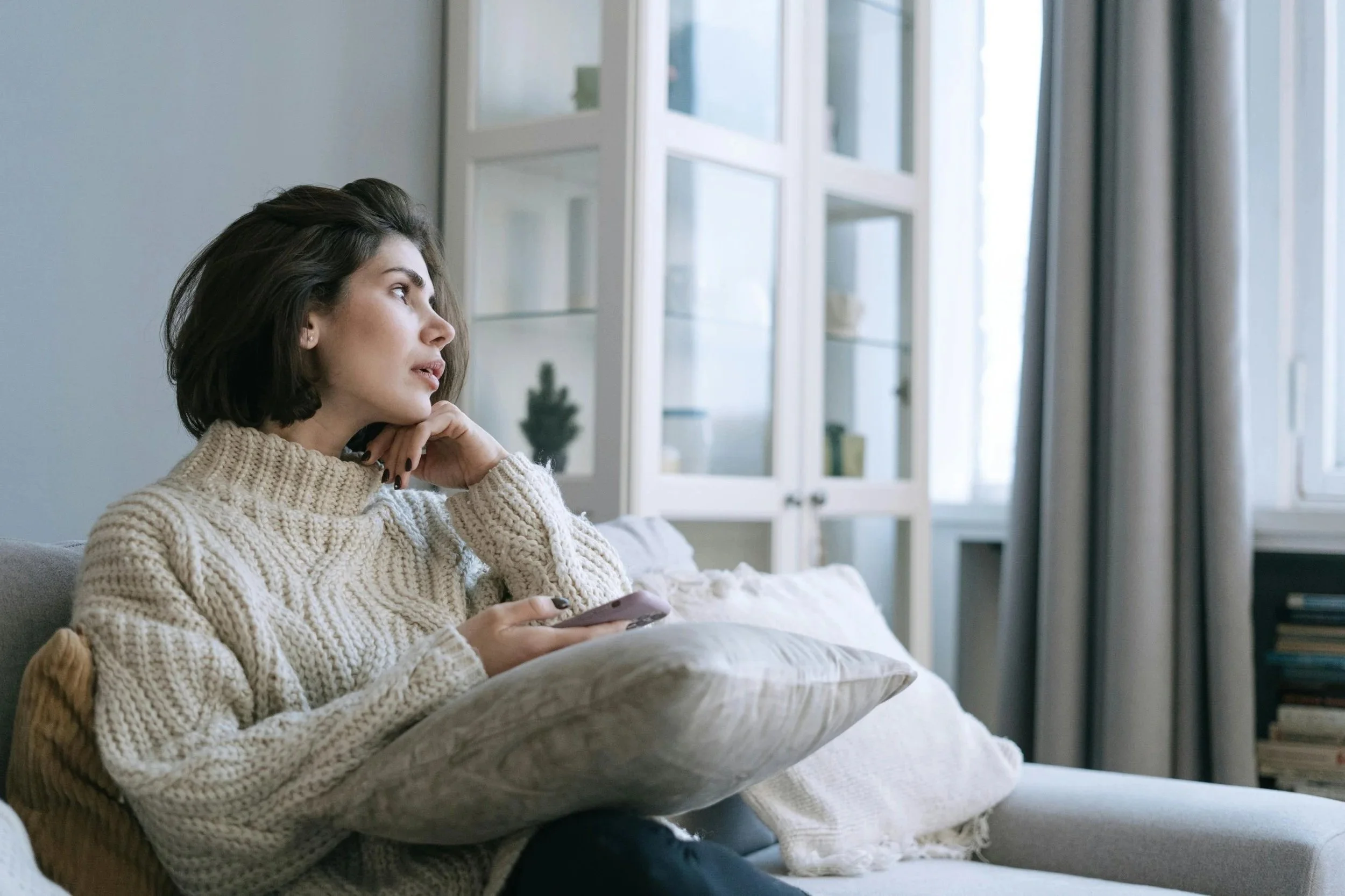 Woman on a couch holding her phone looking thoughtful, OCD therapy in New York