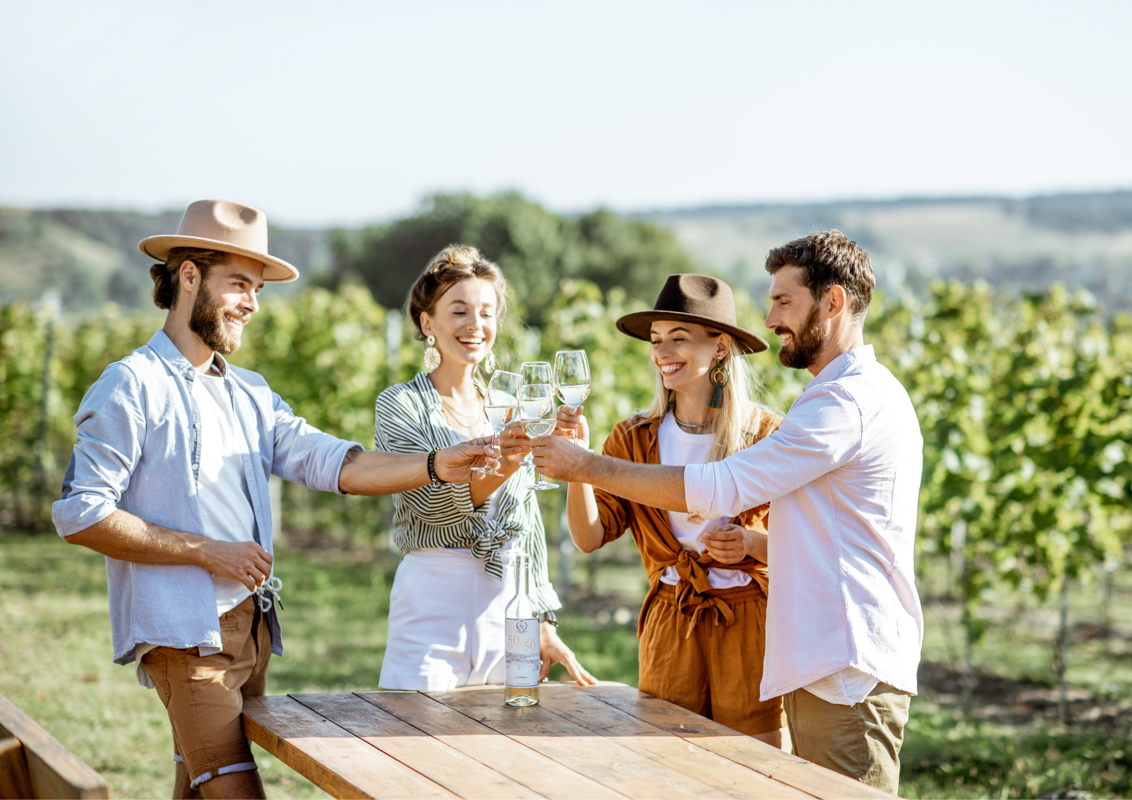 Four friends toasting with white wine glasses in a vineyard.