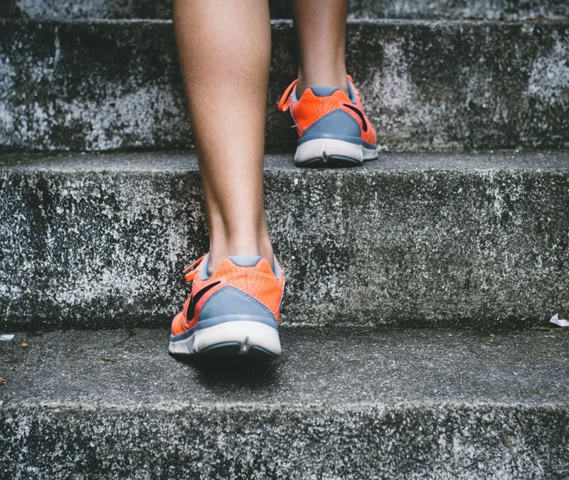 Person wearing orange and gray running shoes walking up concrete stairs.
