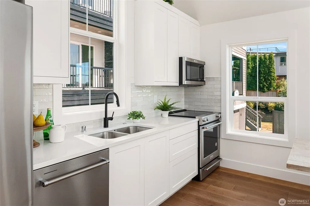 Bright modern kitchen with white cabinets, stainless steel appliances, a black faucet, and a large window with an outdoor view.