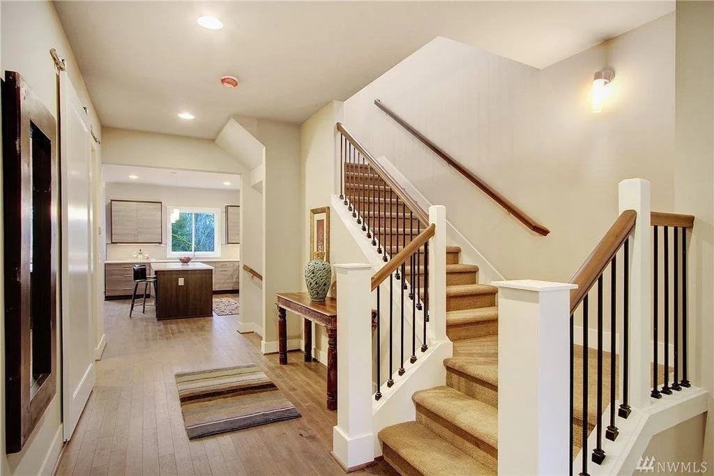View of an interior home entry with staircase on the right, hallway leading to the kitchen, hardwood floors, and a window in the kitchen area.