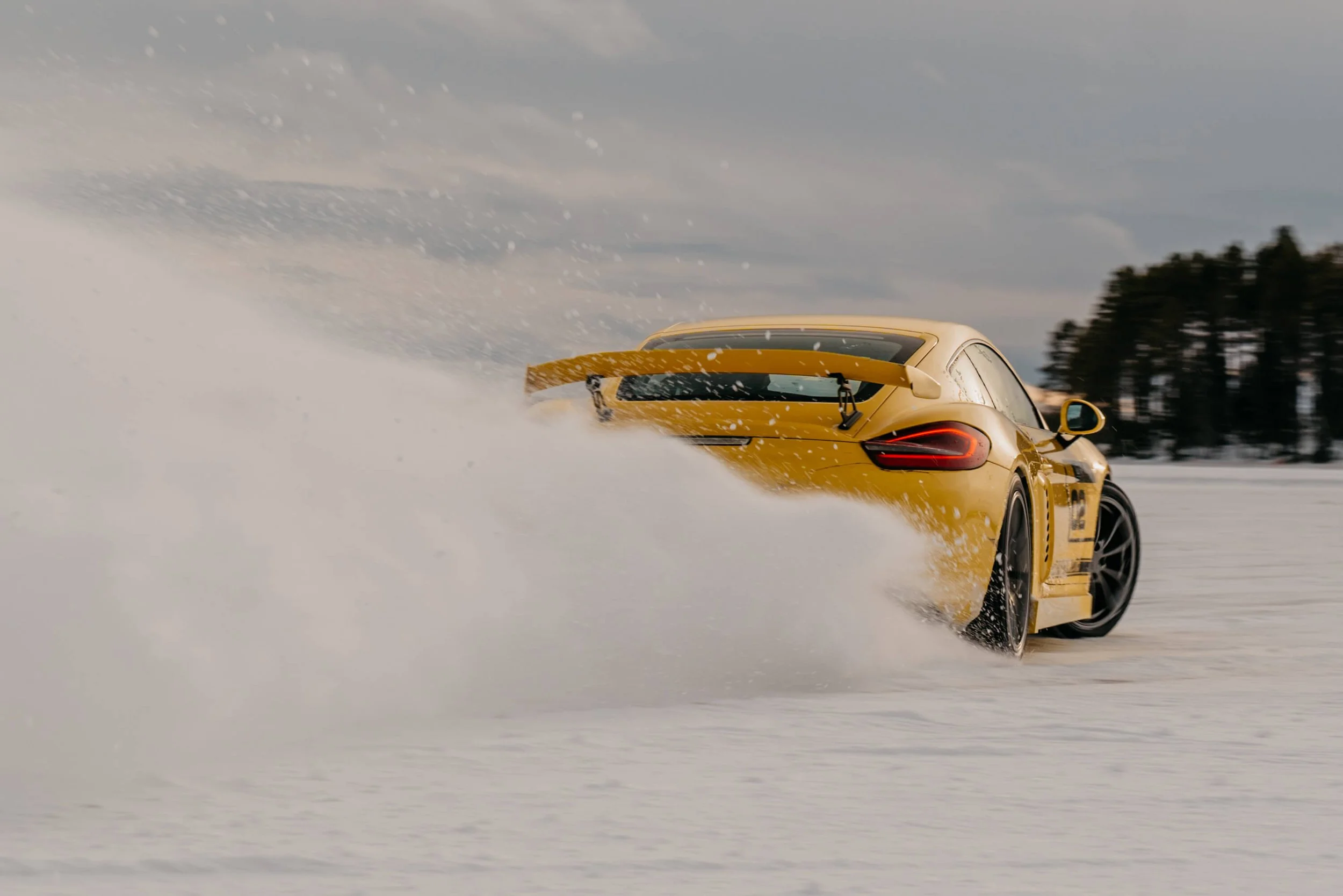 Rear shot of a yellow porsche drifting and spraying camera with snow.