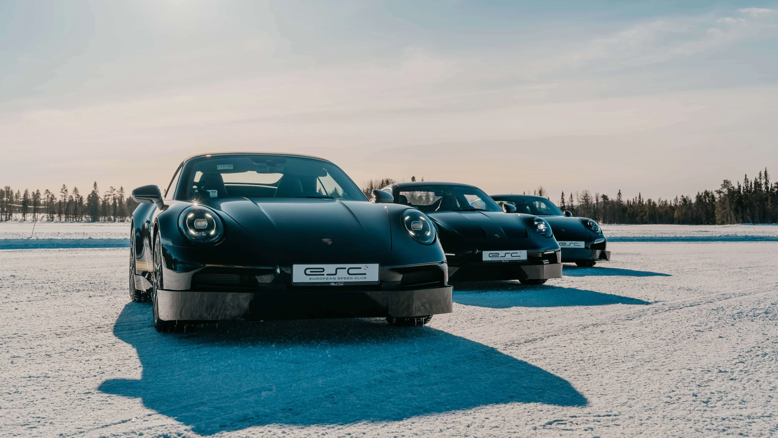 Black porsches parked in diagonal line on frozen lake during sunny day.