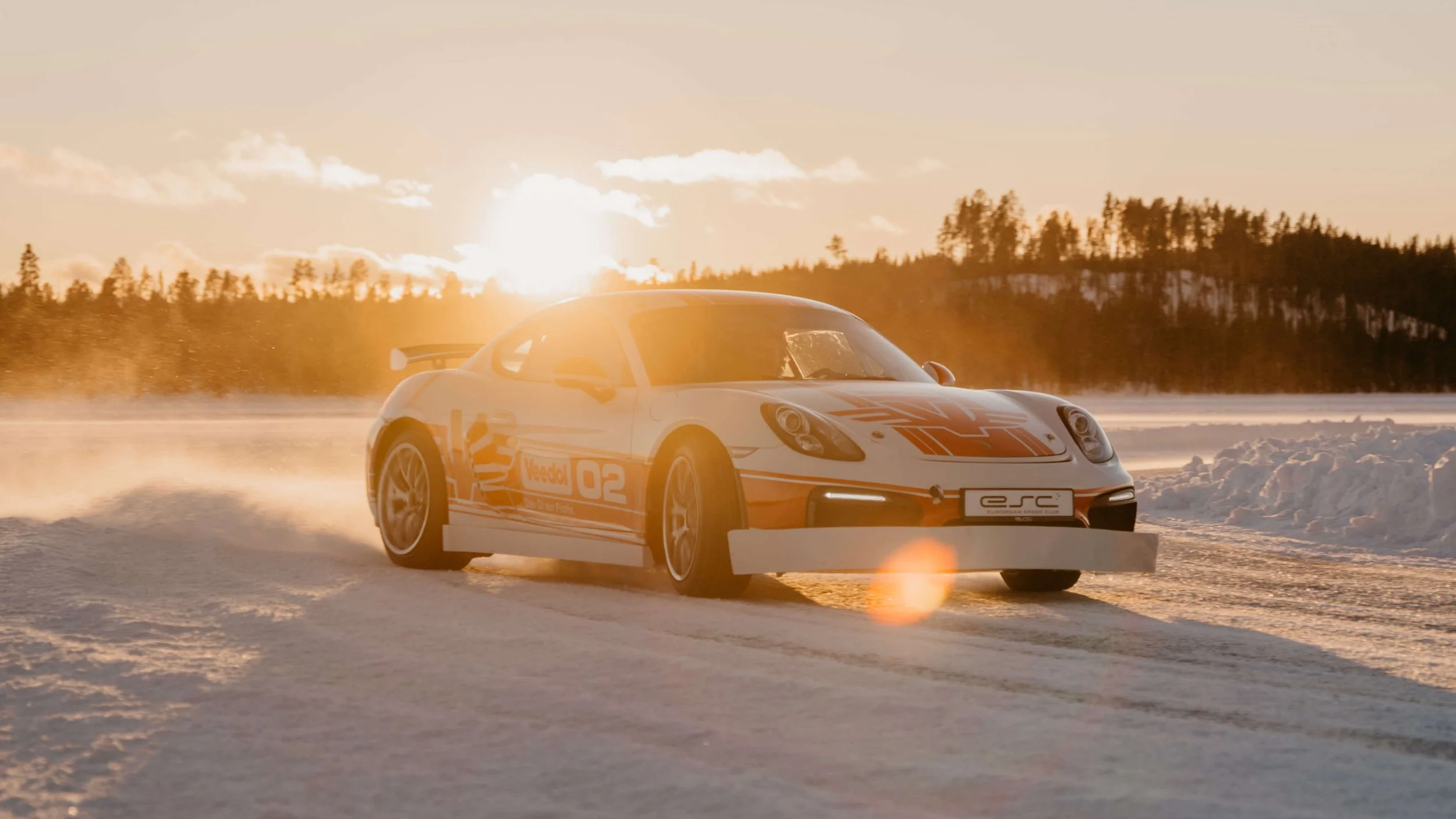 Porsche drifting across a frozen lake with snow spray during golden hour.