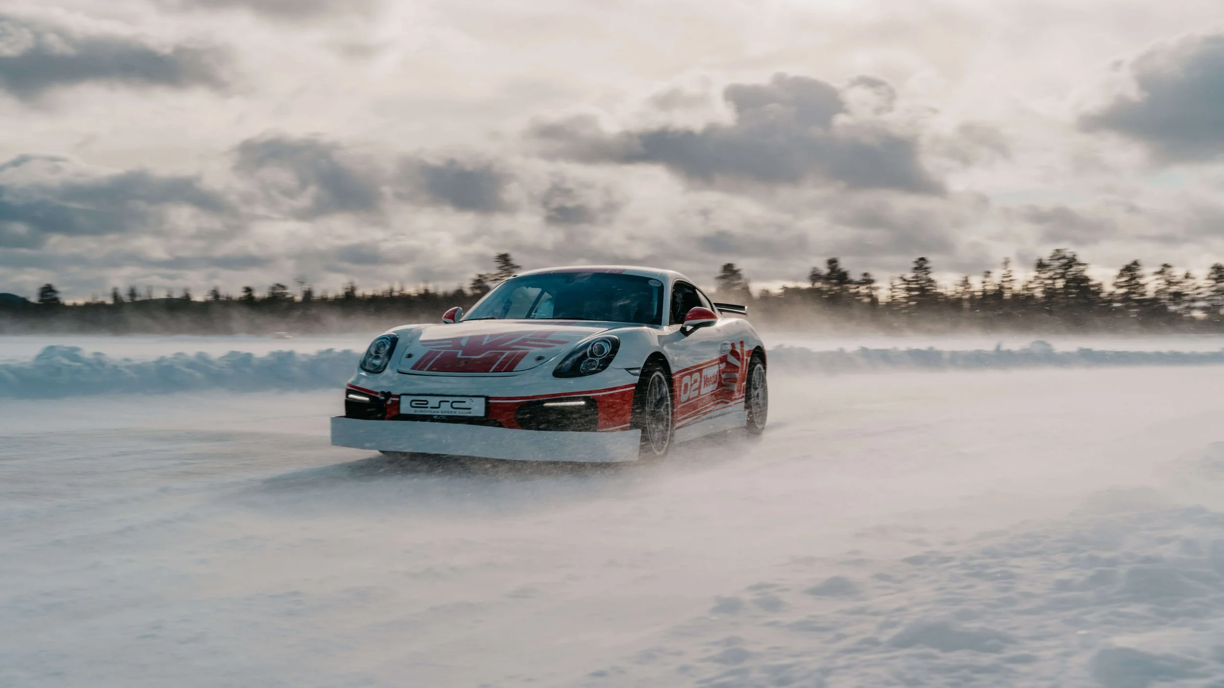 Porsche drifting on snow-covered ice with snow spray and winter landscape.
