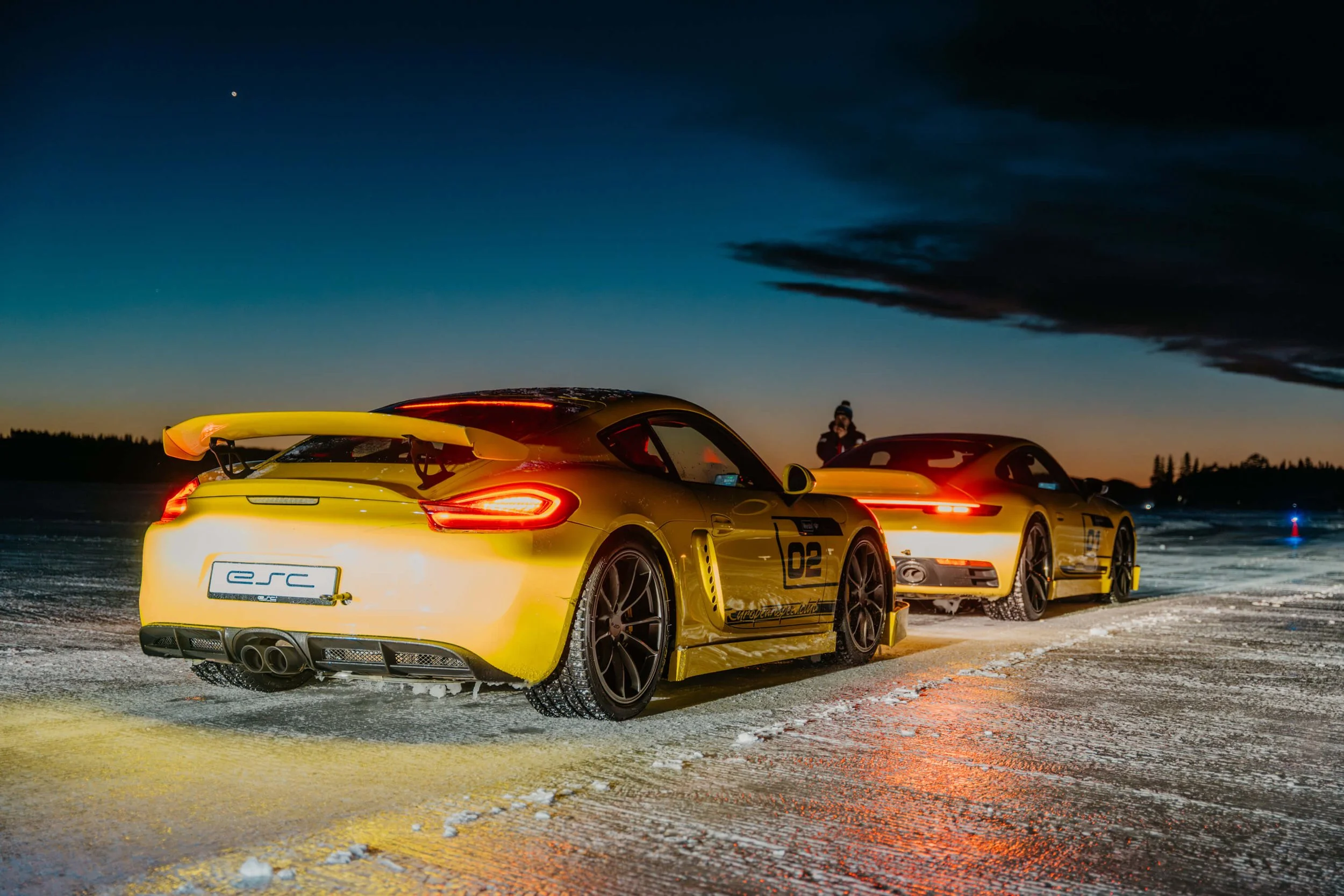 Two porsches waiting at starting line at night with dusk in background.