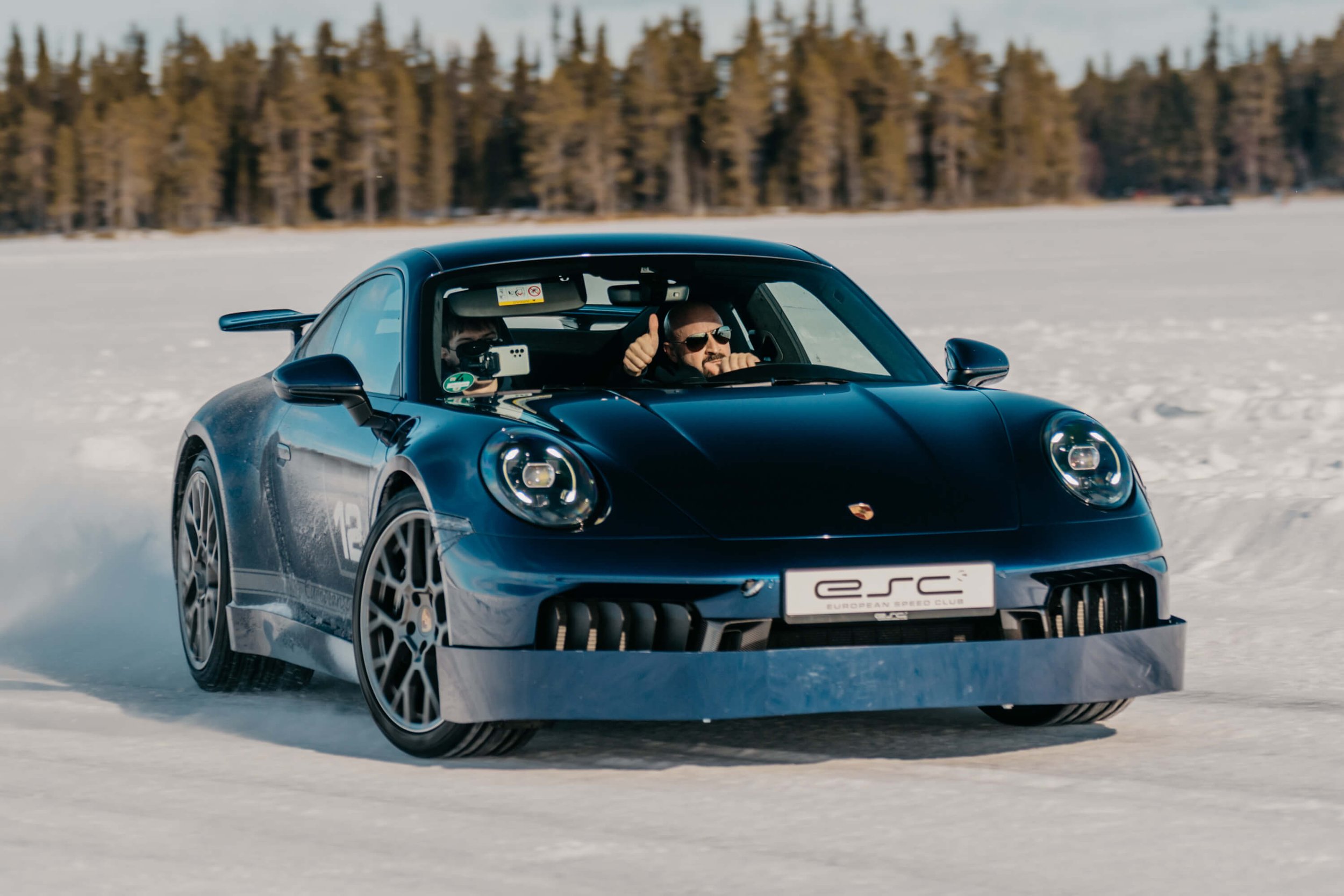 Frontal shot of a porsche drifting with driver giving thumbs up to the camera.