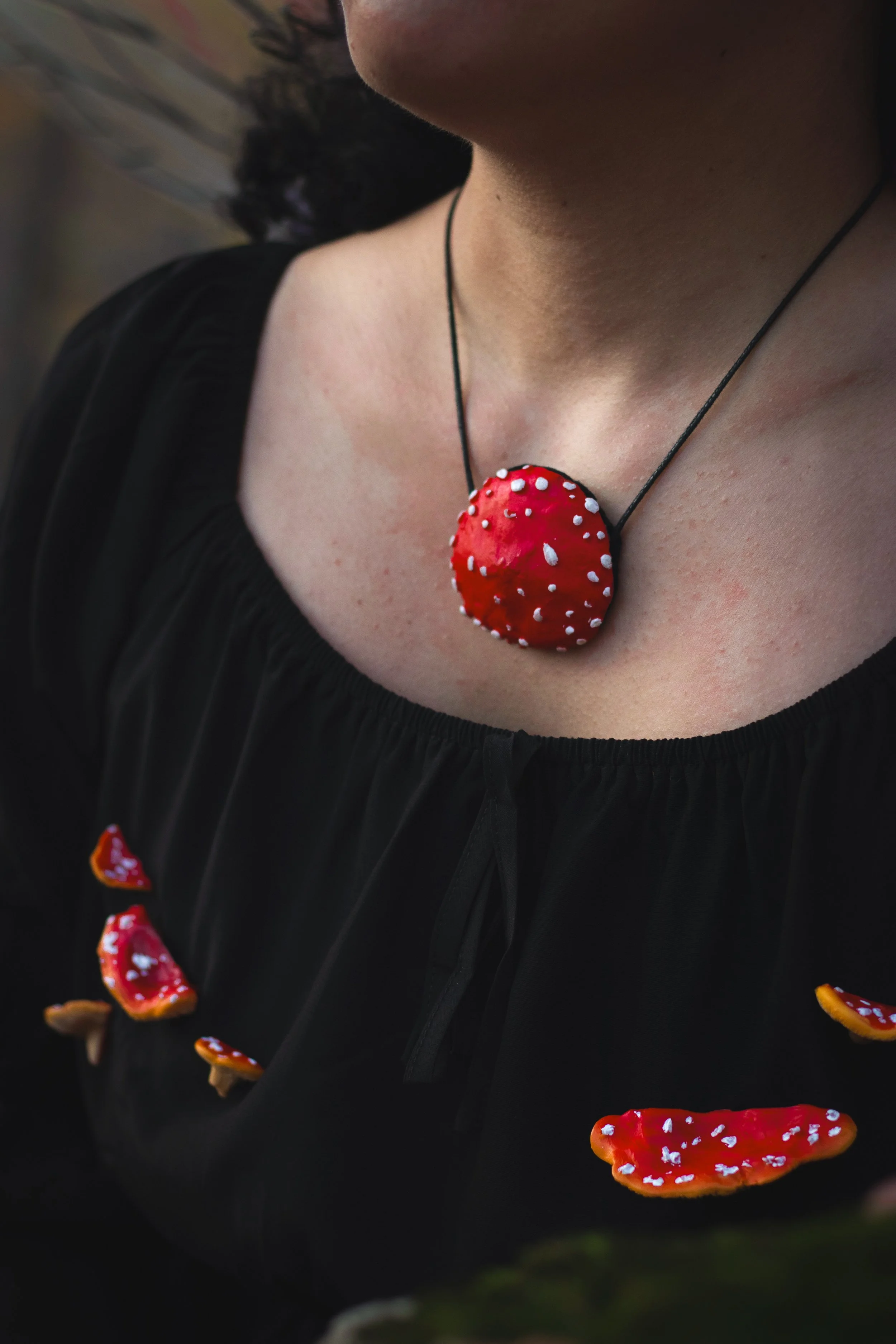 Una persona indossa una collana e un abito nero decorato con pezzi di funghi rossi con puntini bianchi, che sembrano funghi velenosi.