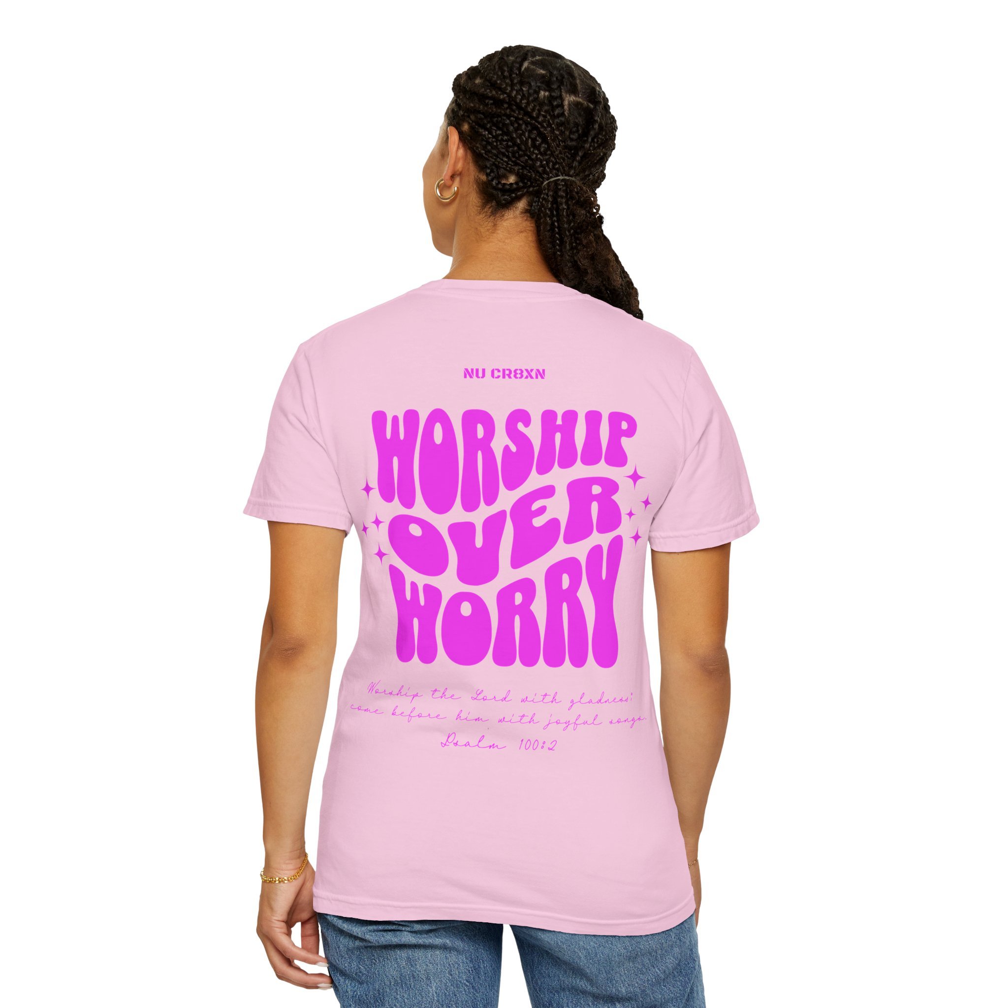 Back of a woman with braided hair wearing a pink T-shirt with pink text 'WORSHIP OVER WORRY' and religious scripture underneath.