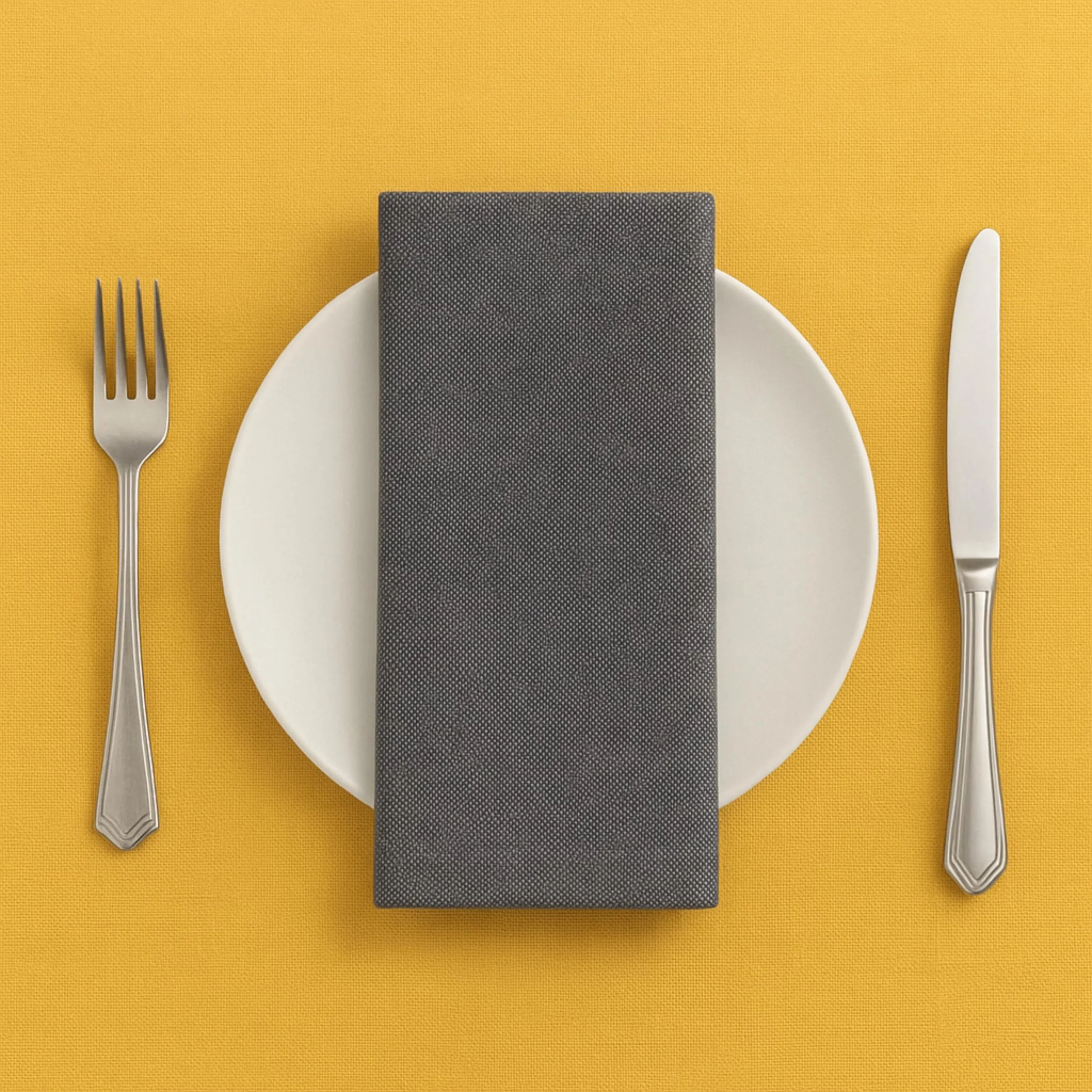 A dining table setting with a white round plate, a gray textured napkin on the plate, a fork on the left, and a knife on the right, all on a yellow tablecloth.