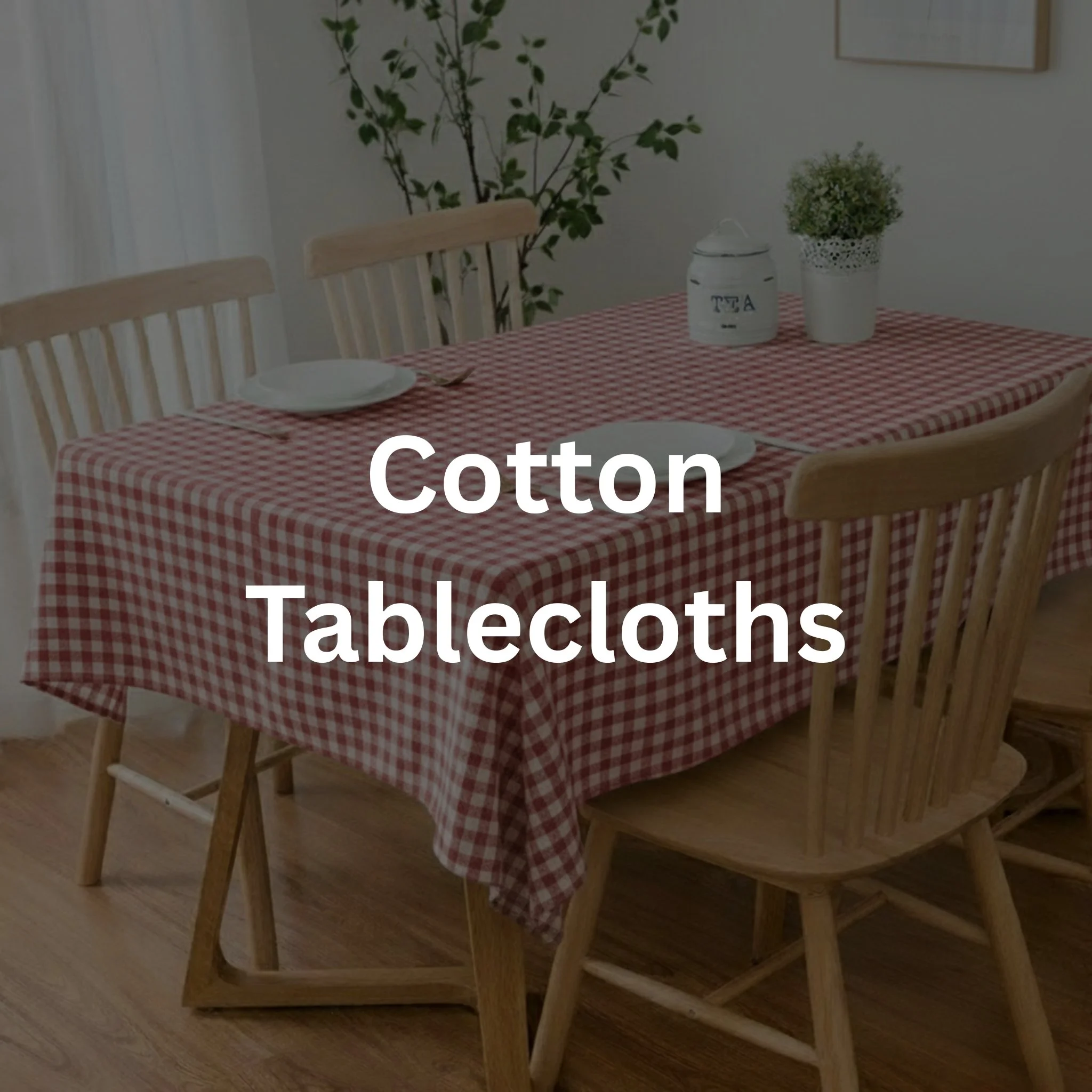 Wooden dining table with a red and white checkered tablecloth, surrounded by wooden chairs, set with white plates and cutlery, with a potted plant and a white container marked "TEA" in the background.
