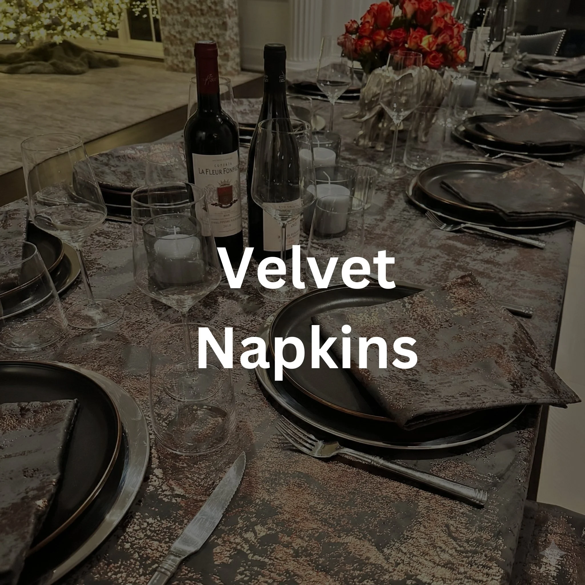 A dining table set with dark velvet napkins, wine glasses, wine bottles, candles, plates, and cutlery, with a floral centerpiece in the background.