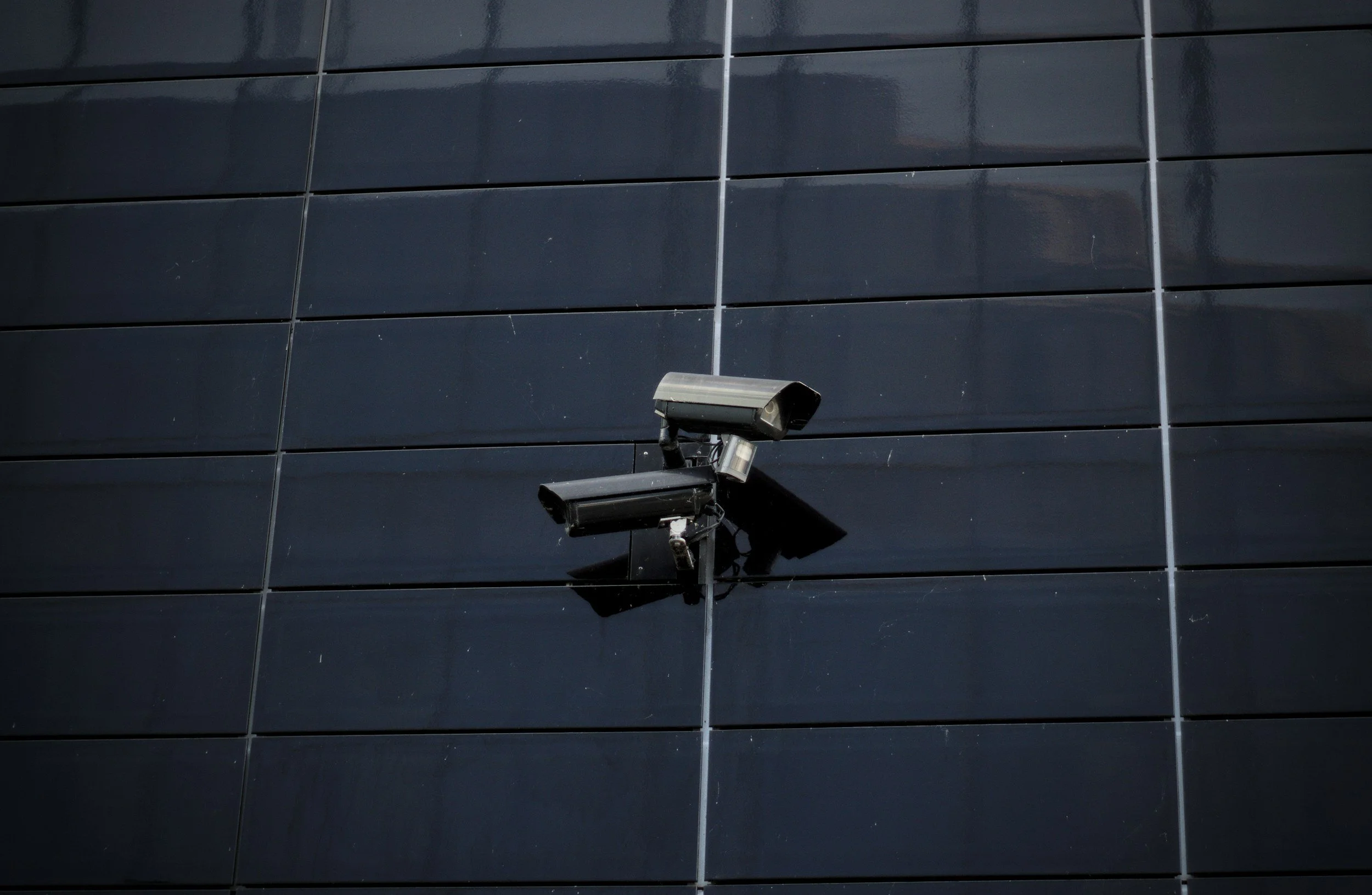 Two security cameras mounted on a black glass building exterior.