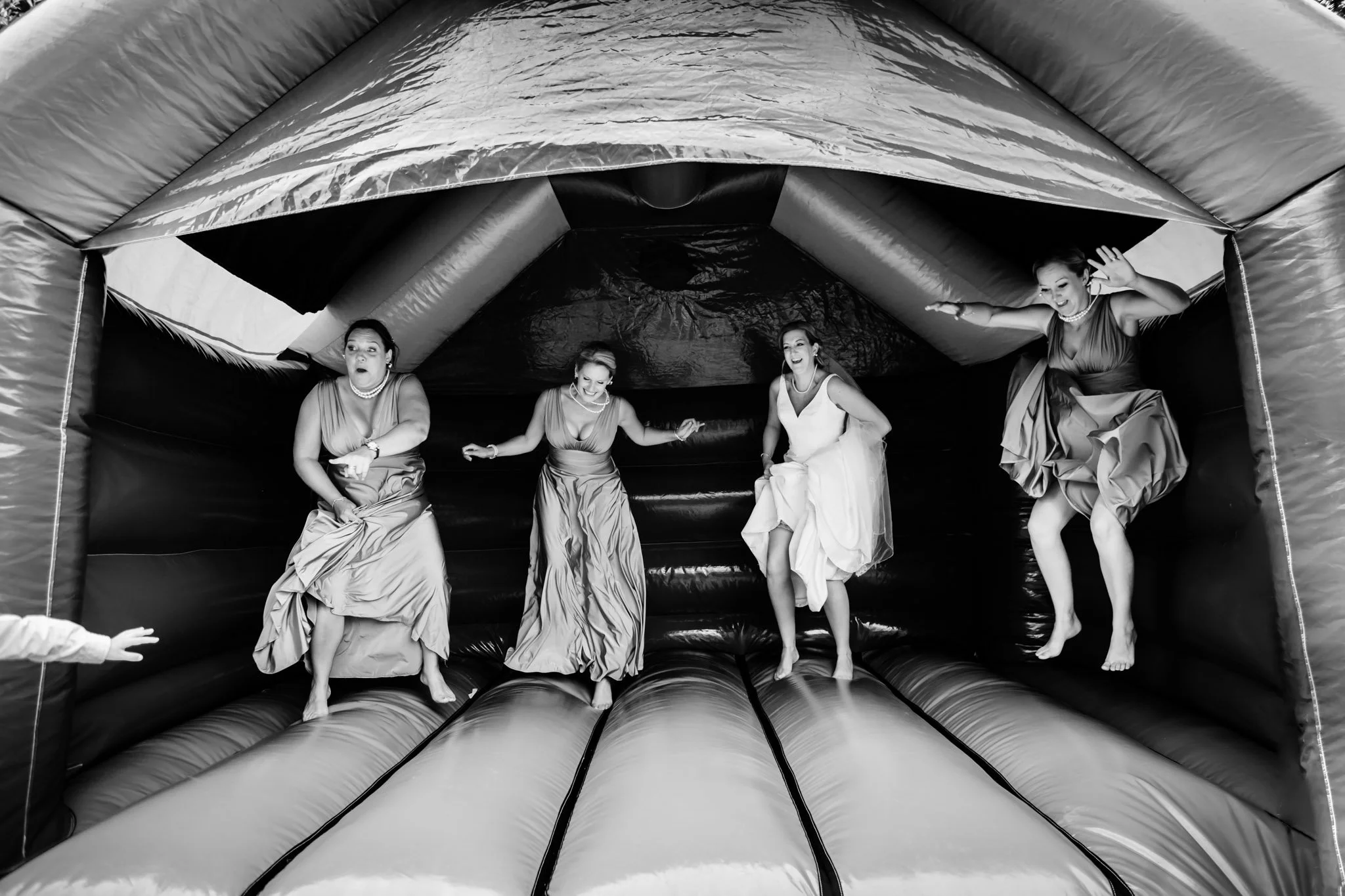 Four women in dresses jumping on a bouncy house at a celebration or event.