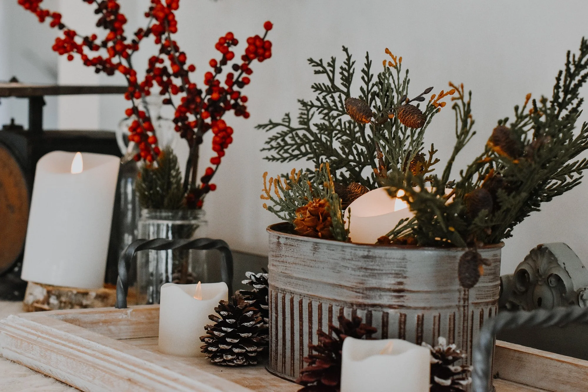 upclose holiday metal farmhouse decor, candles, holly berry, ferns and greenery, pine conees in canister on tray in rustic farmhouse stay rental
