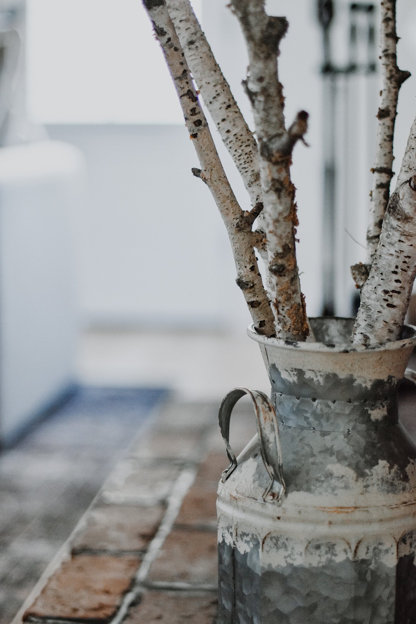 upclose birch branches in metal farmhouse canister on the foot of a brick fireplace in rustic farmhouse stay rental