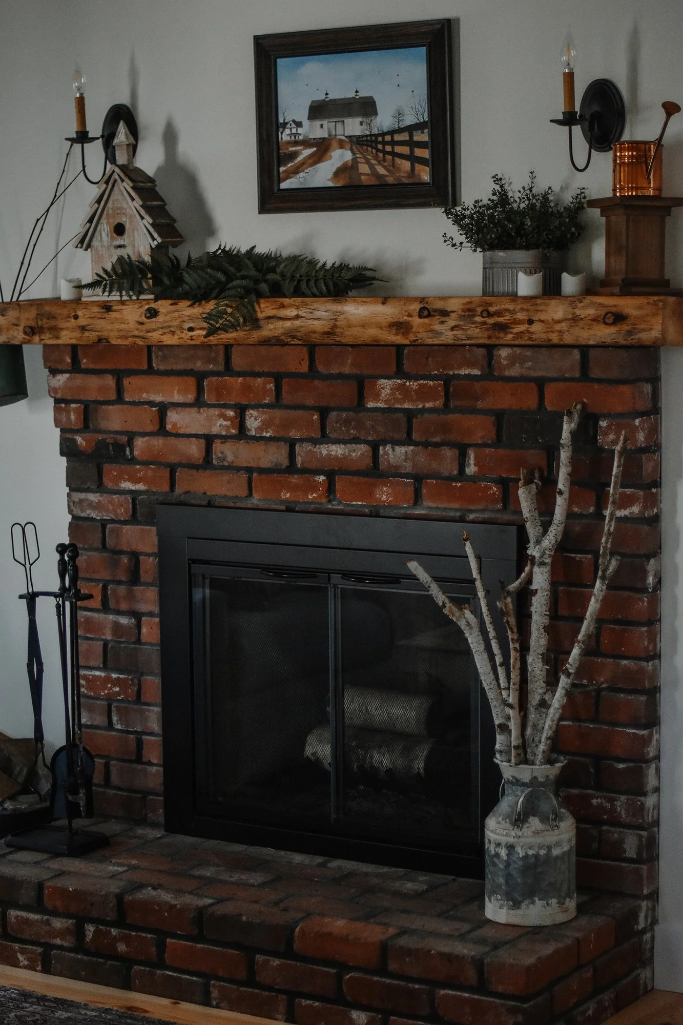 1890 restored farmhouse entry room with original wood burning fireplace, birch branches in metal milk container, candelstick lights, and greenry on the reclaimed antique wood mantal in farmhouse stay