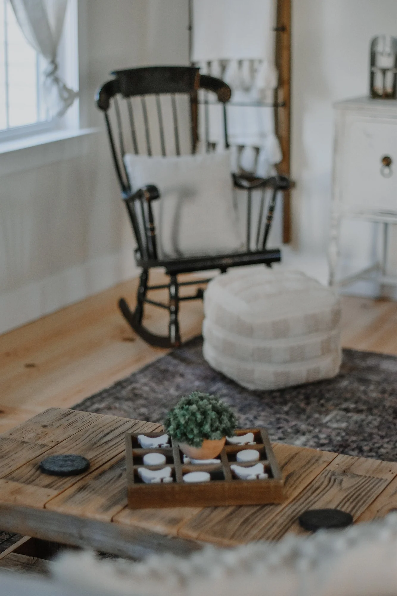 1890 restored farmhouse rental sititng room featuring antique and modern farmhouse decor. Rocking chair with cotton ottoman and pillow, blanket ladder, antique buffet, next to a window with natural light pouring in. Rustic wooden coffee table with fa