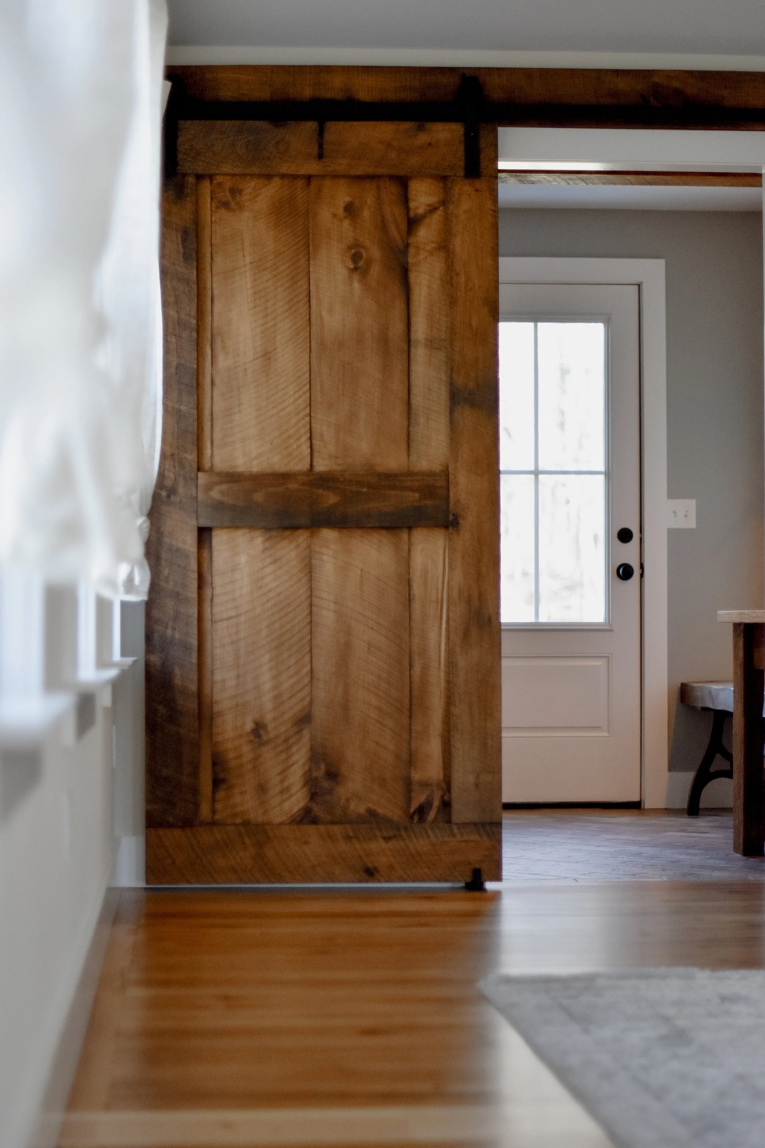 rustic modern farmhouse refurbished rustic sliding barn door, backdoor entrance peeking behind barn door, dining room with creamy curtains, and restored original 1890 floors