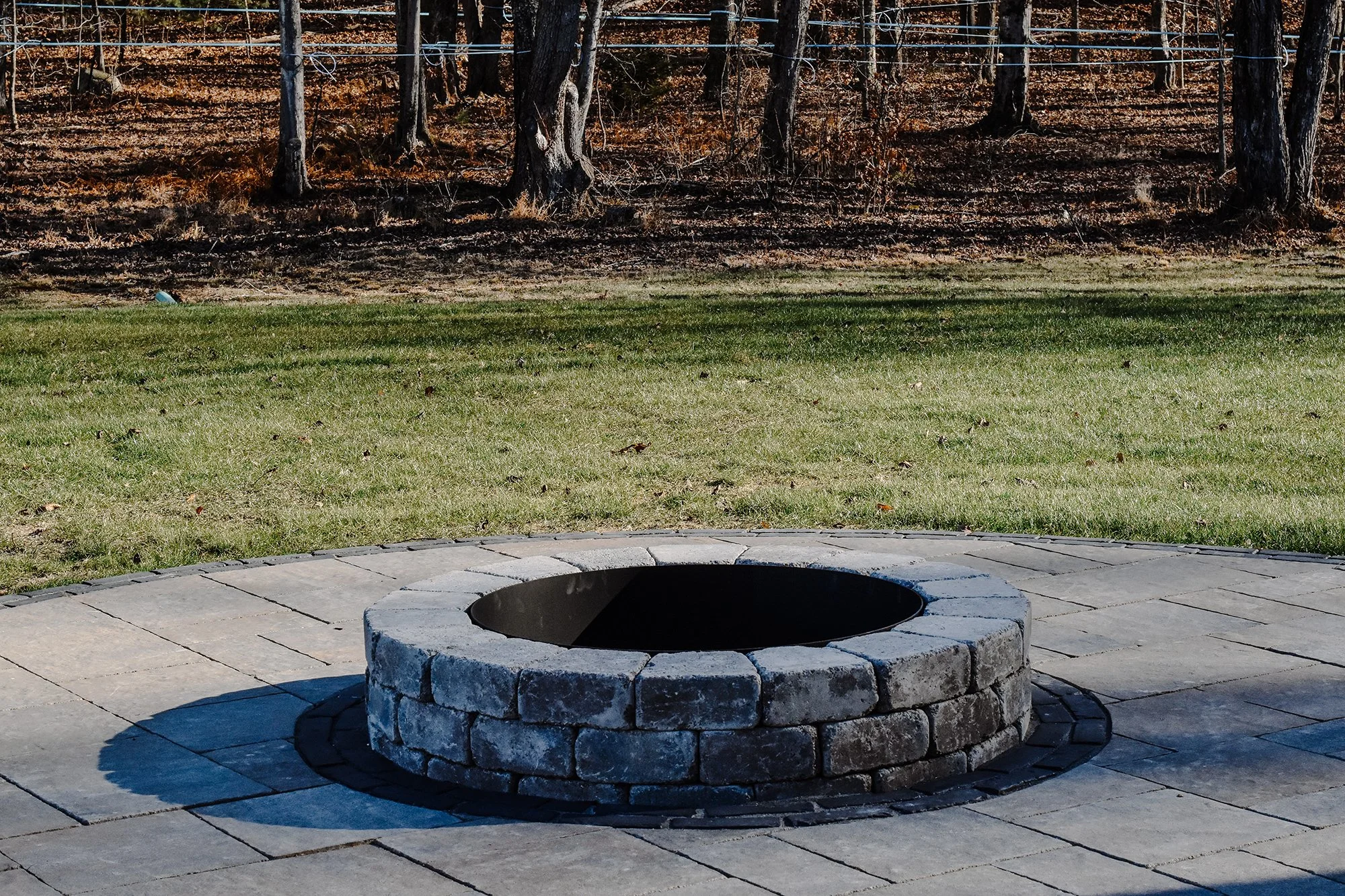 outdoor stone concrete patio for outdoor gathering sourronded by grass and maple trees behind