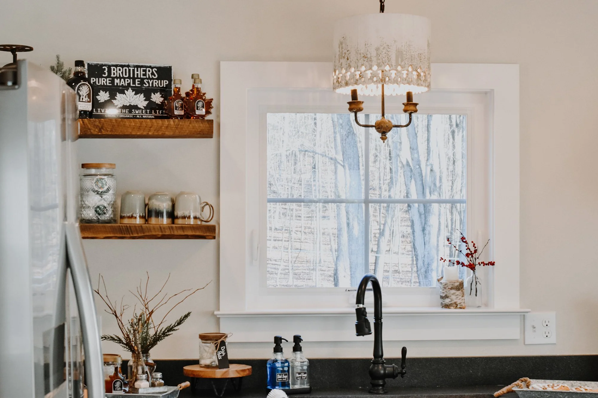 1890 restored farmhouse stay kitchen with modern and rustic details, creamy white, antique chandelier, reclaimed wood floating shelves, maple syrup bottles, coffee mugs, above the sink window, kitchen sink