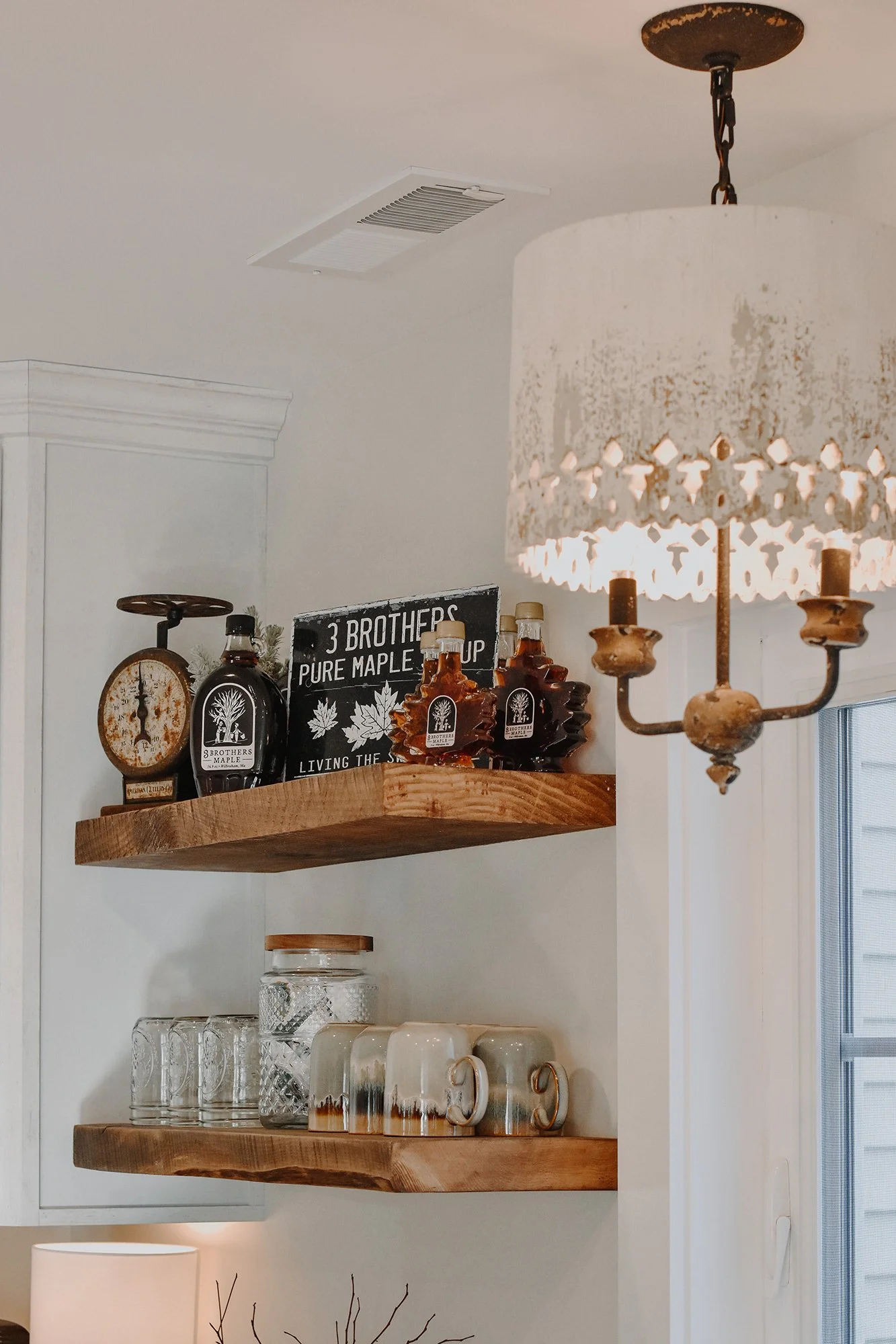 1890 restored farmhouse stay kitchen with modern and rustic details, creamy white, antique chandelier, reclaimed wood floating shelves, maple syrup bottles, coffee mugs, k cups, above the sink window,  rustic antique scale