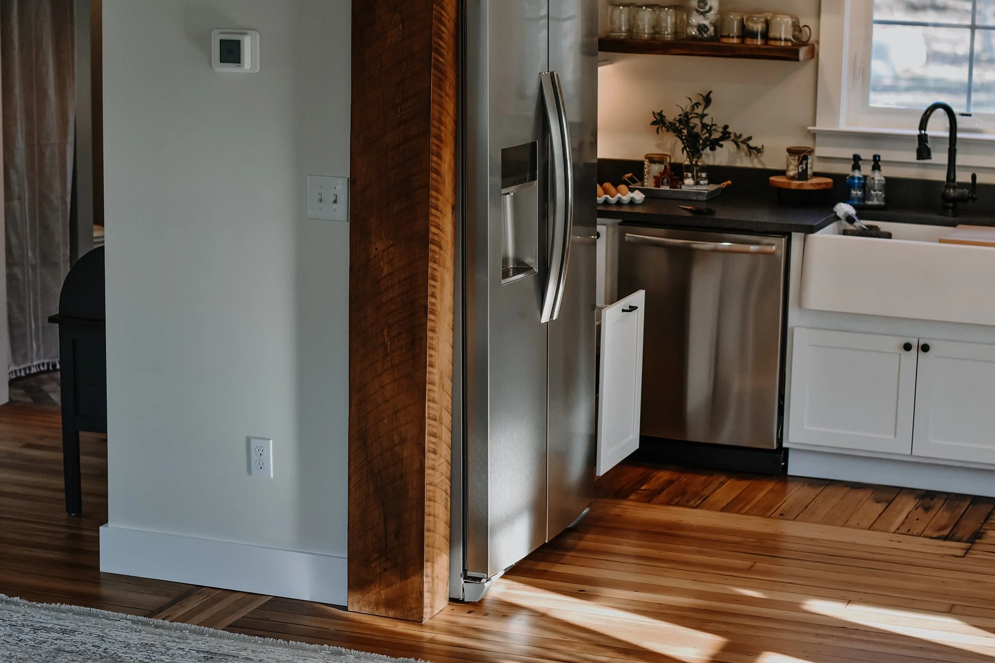 1890 restored farmhouse stay kitchen with modern and rustic details, creamy white paint, natural light pouring through the windows, new cabinets, above the sink window,  modern stainless steel fridge, reclaimed wood beams, restored farmhouse floors
