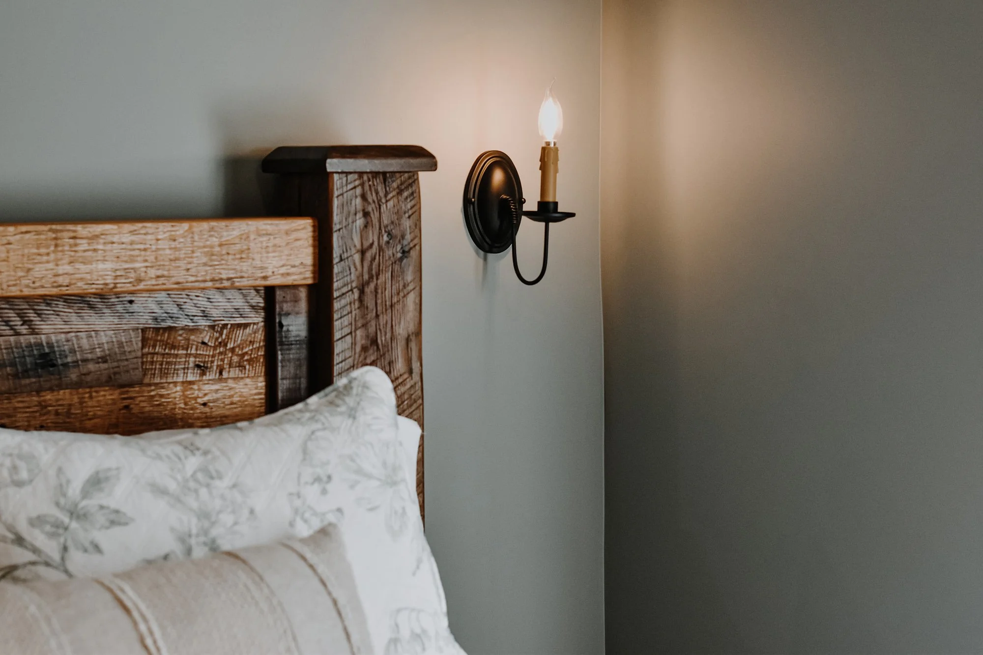 1890 restored farmhouse stay rustic master bedroom with solid wooden handcrafted bedframe, creamy floral bed linen pillows, candlestick light fixtures