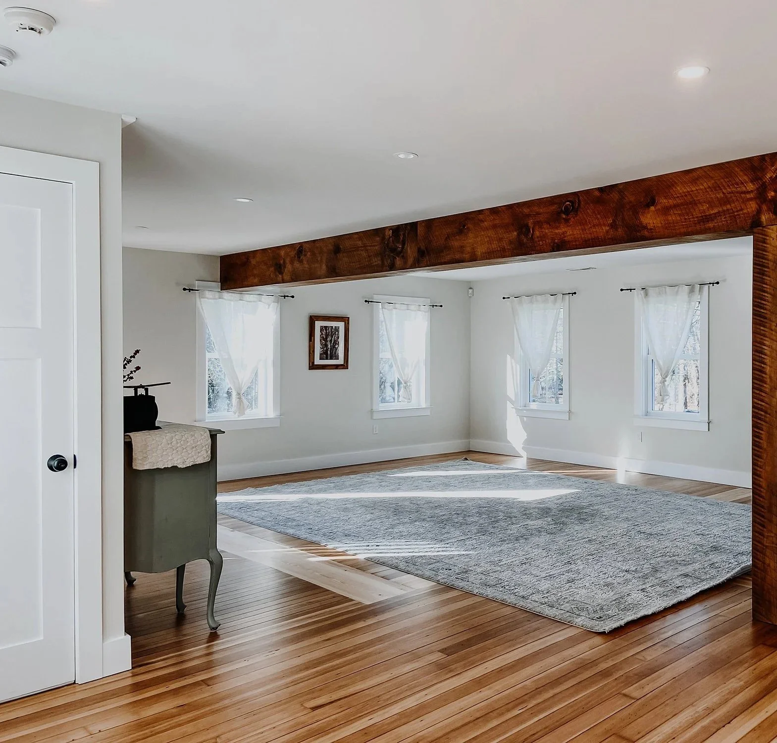 1890 restored farmhouse dining room small gathering space lined with windows pouring in natural light, reclaimed wood beams and refinished original wood floors, rustic rug and anitque accents