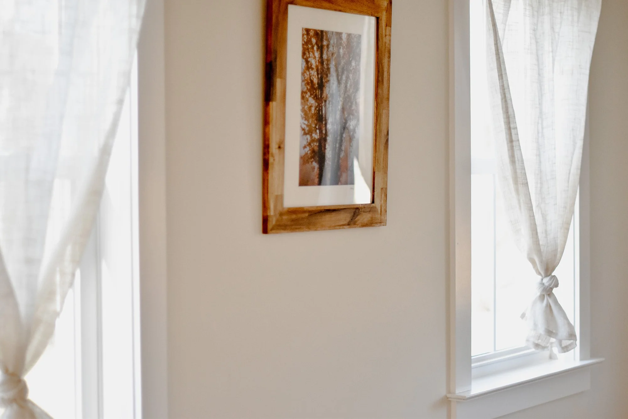 modern farmhouse stay, natural light puring in through two windows and a suage maple photo i wooden frame hung on the creamy white wall 