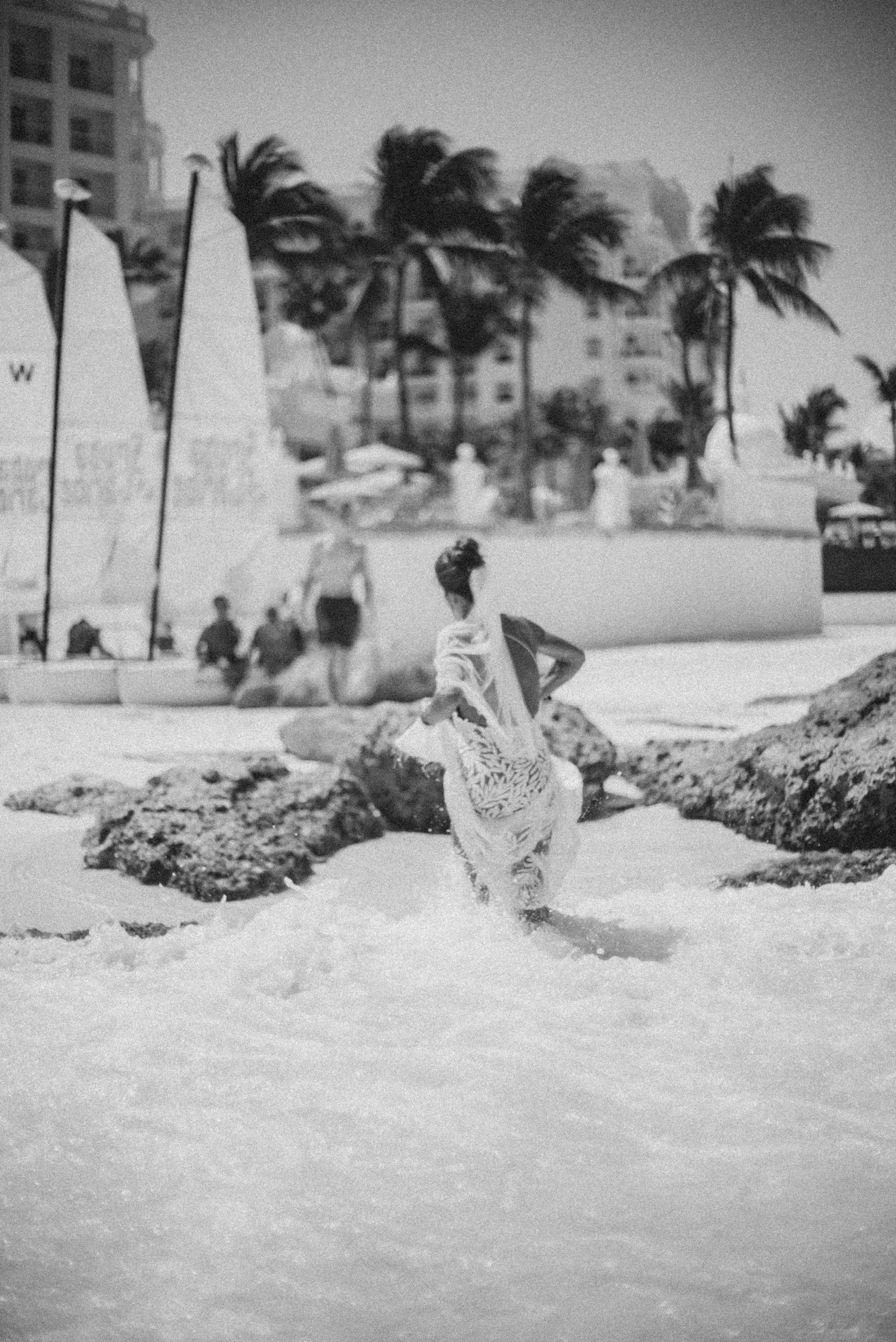 A person running on a snowy beach with large rocks and palm trees in the background, in black and white.