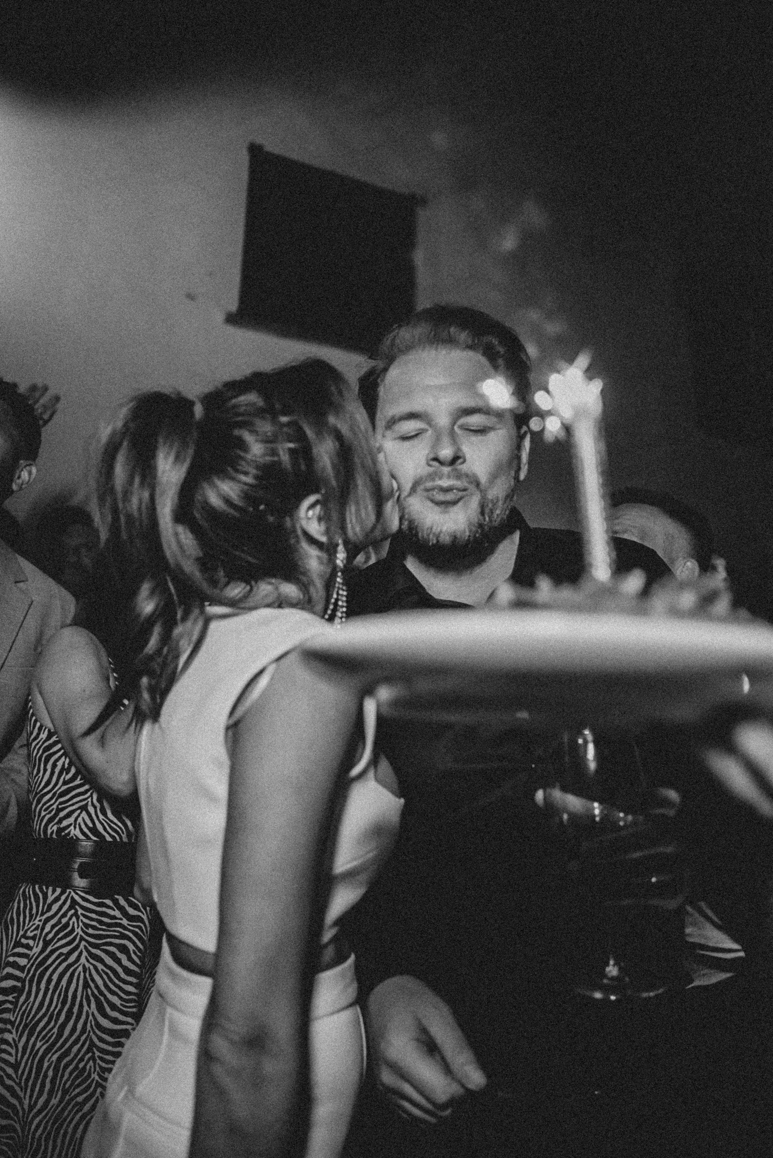 People at a party, with a woman in zebra print and a man with a beard, holding a drink, smiling.