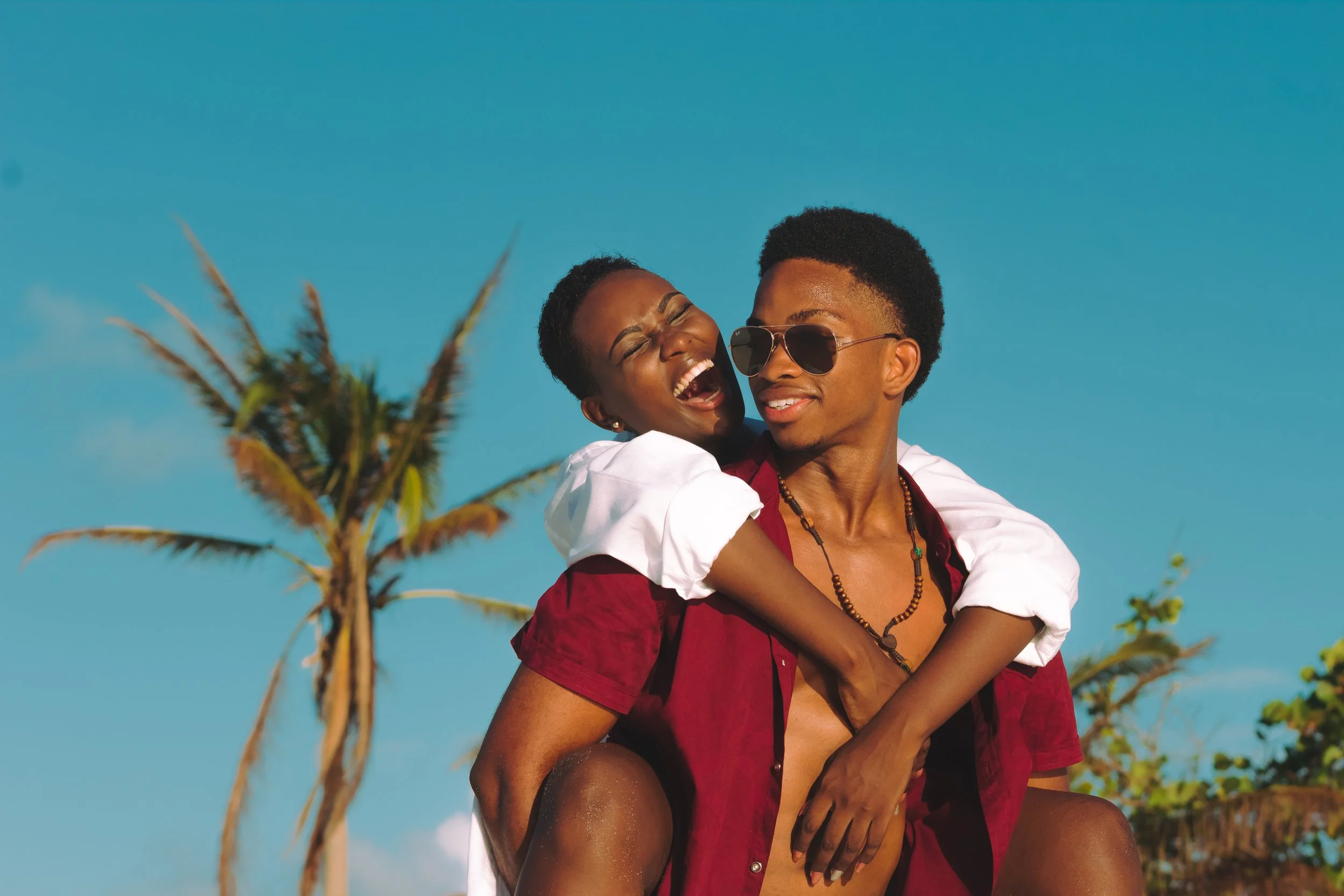 A joyful couple enjoying a moment outdoors on a sunny day, with palm trees and a clear blue sky in the background.
