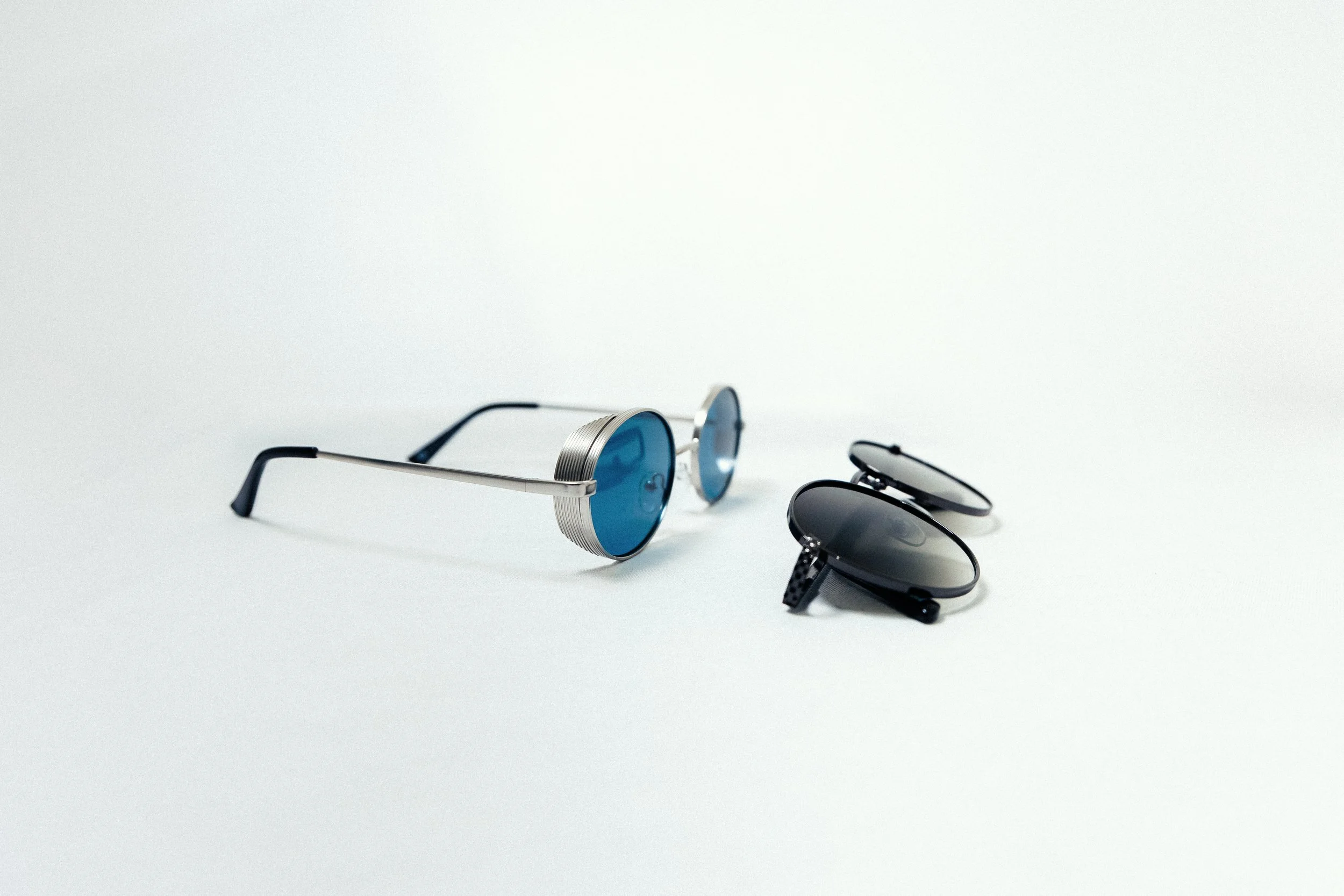 Pair of sunglasses with blue lenses and another pair with dark lenses on a white background.