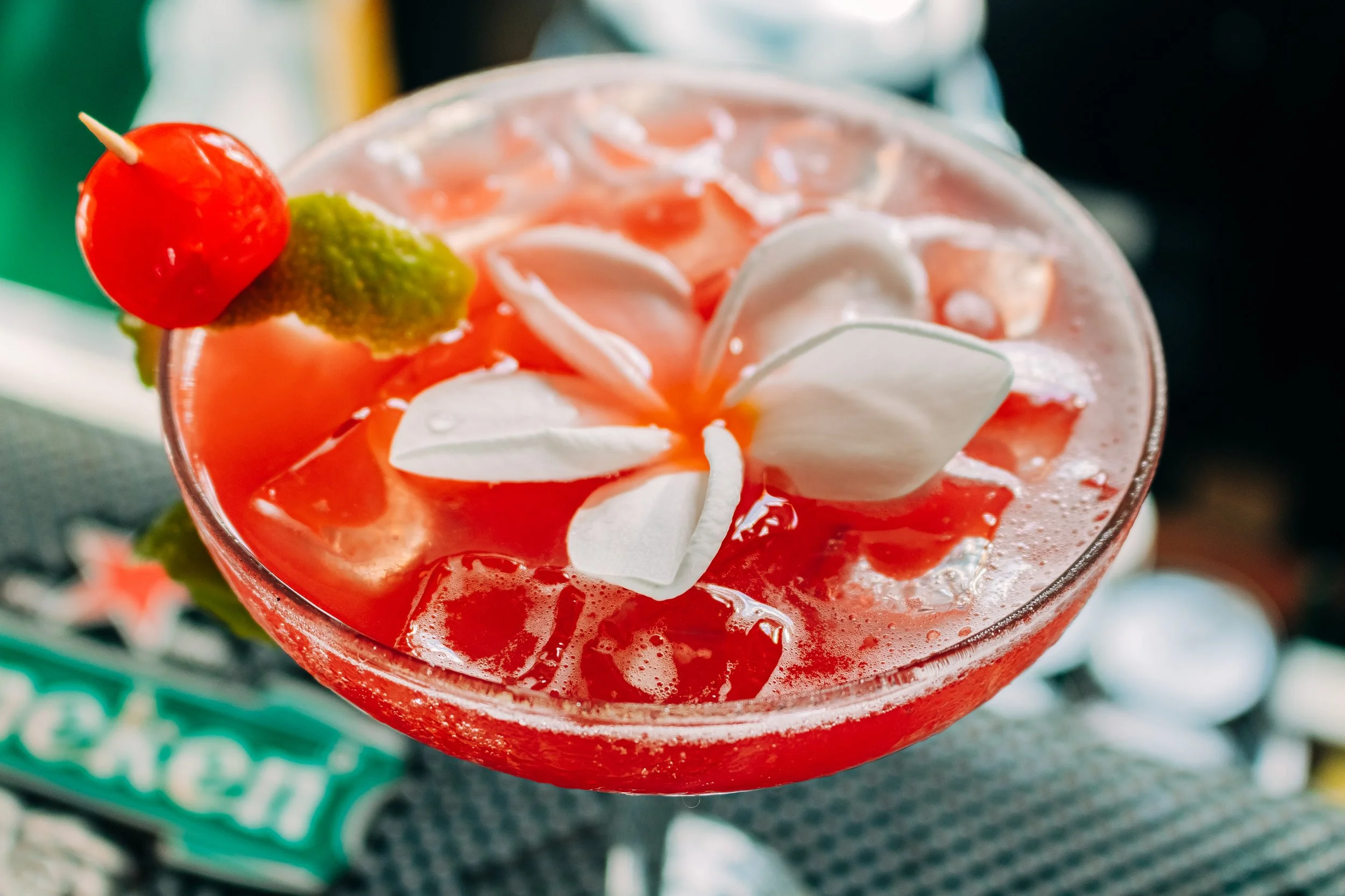 Close-up of a colorful cocktail with whipped cream, a cherry, and a lime wedge on the rim of the glass.