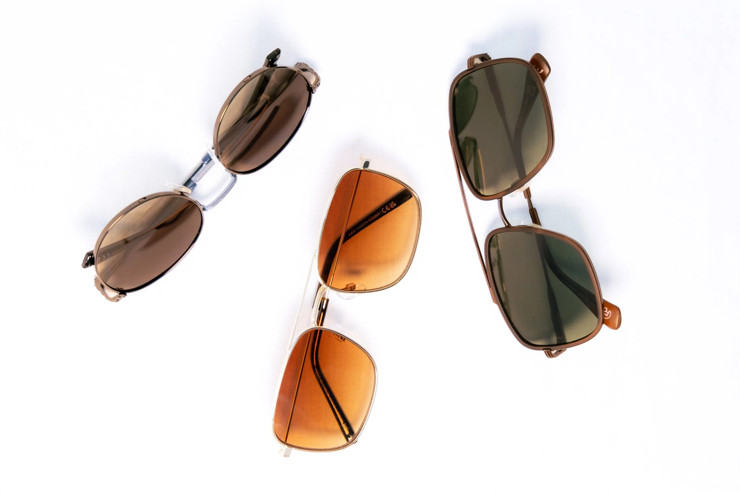 Three pairs of sunglasses with different frames and lens colors arranged on a white surface.