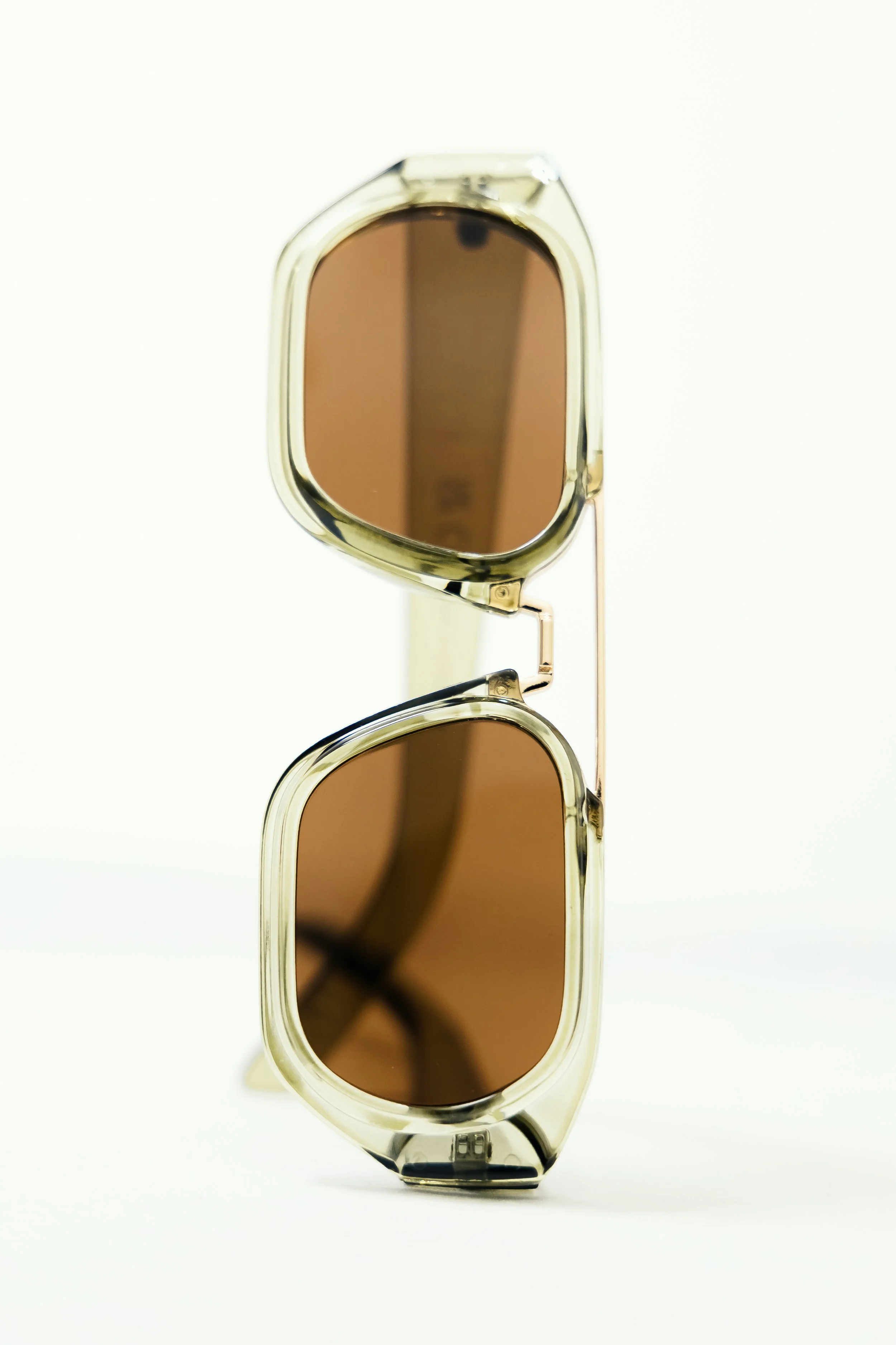 A pair of sunglasses with a tan frame and brown lenses, positioned vertically with the fold hinge showing.