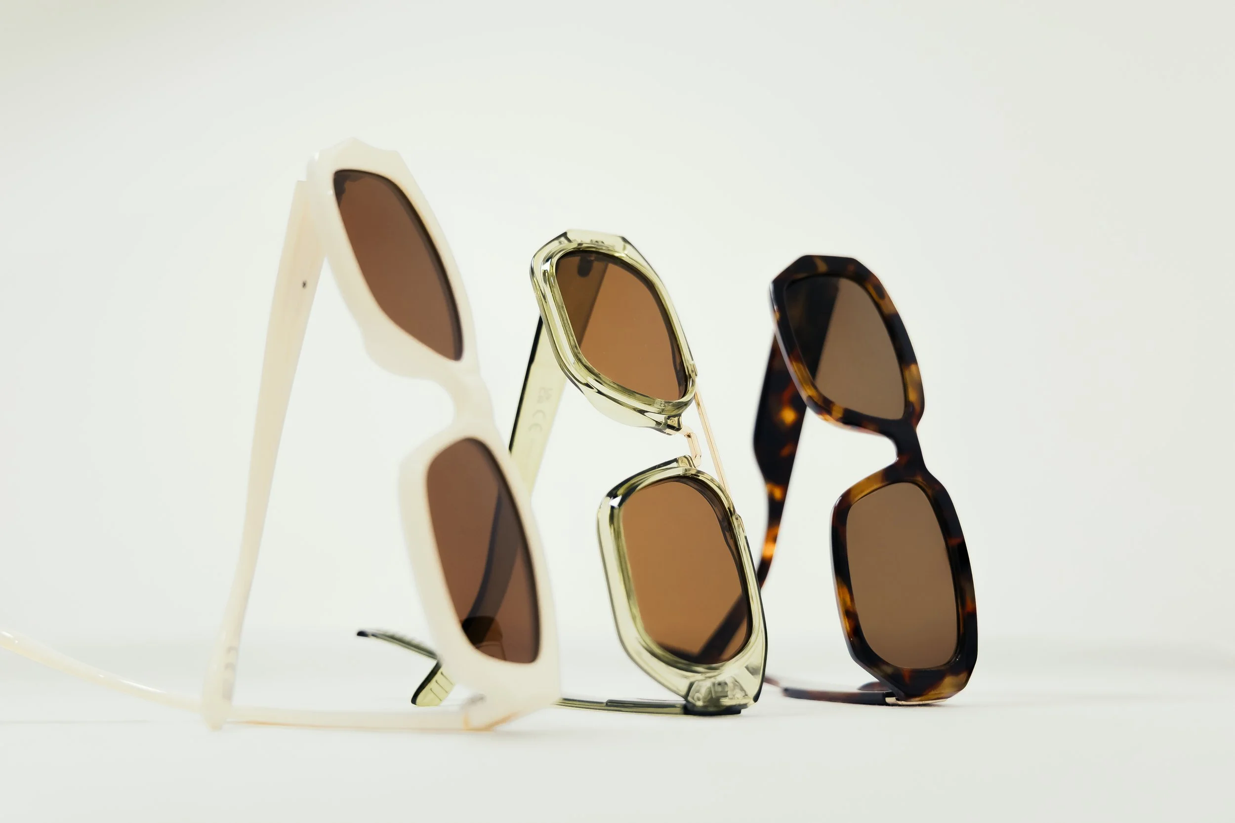 Three pairs of sunglasses with different frame styles and colors on a white surface.