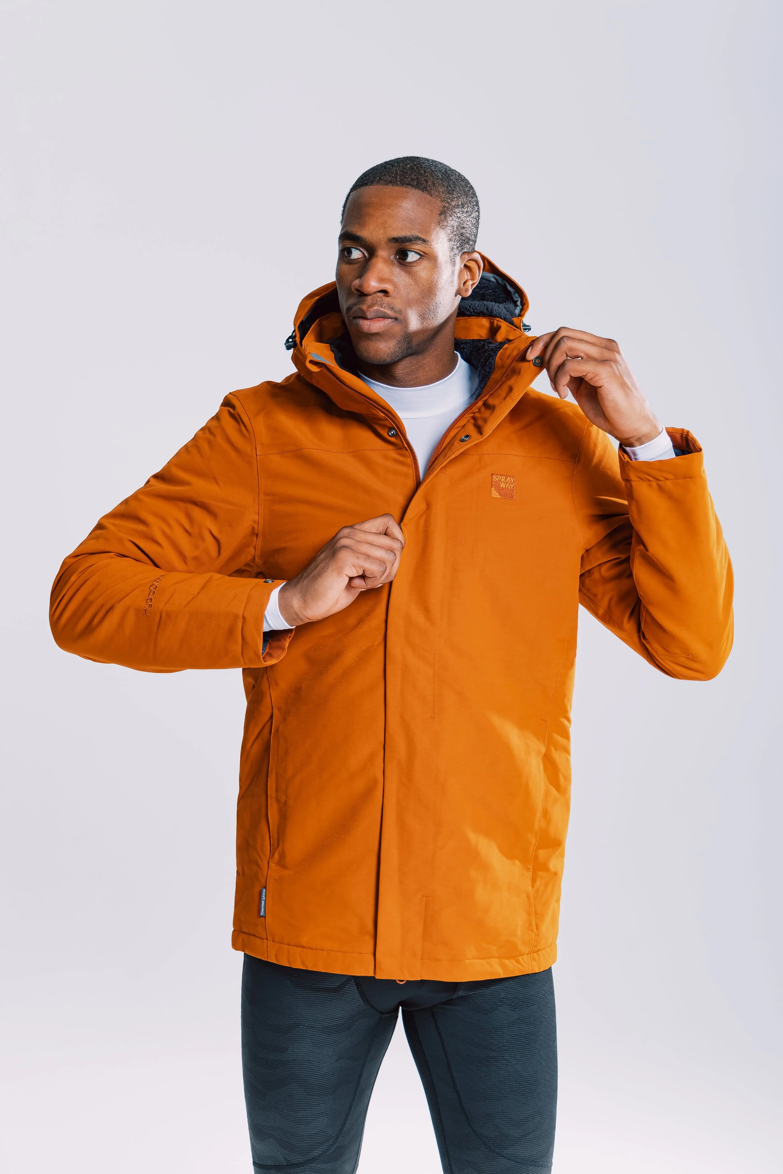 A man in an orange outdoor jacket adjusting its collar, standing against a plain light background.