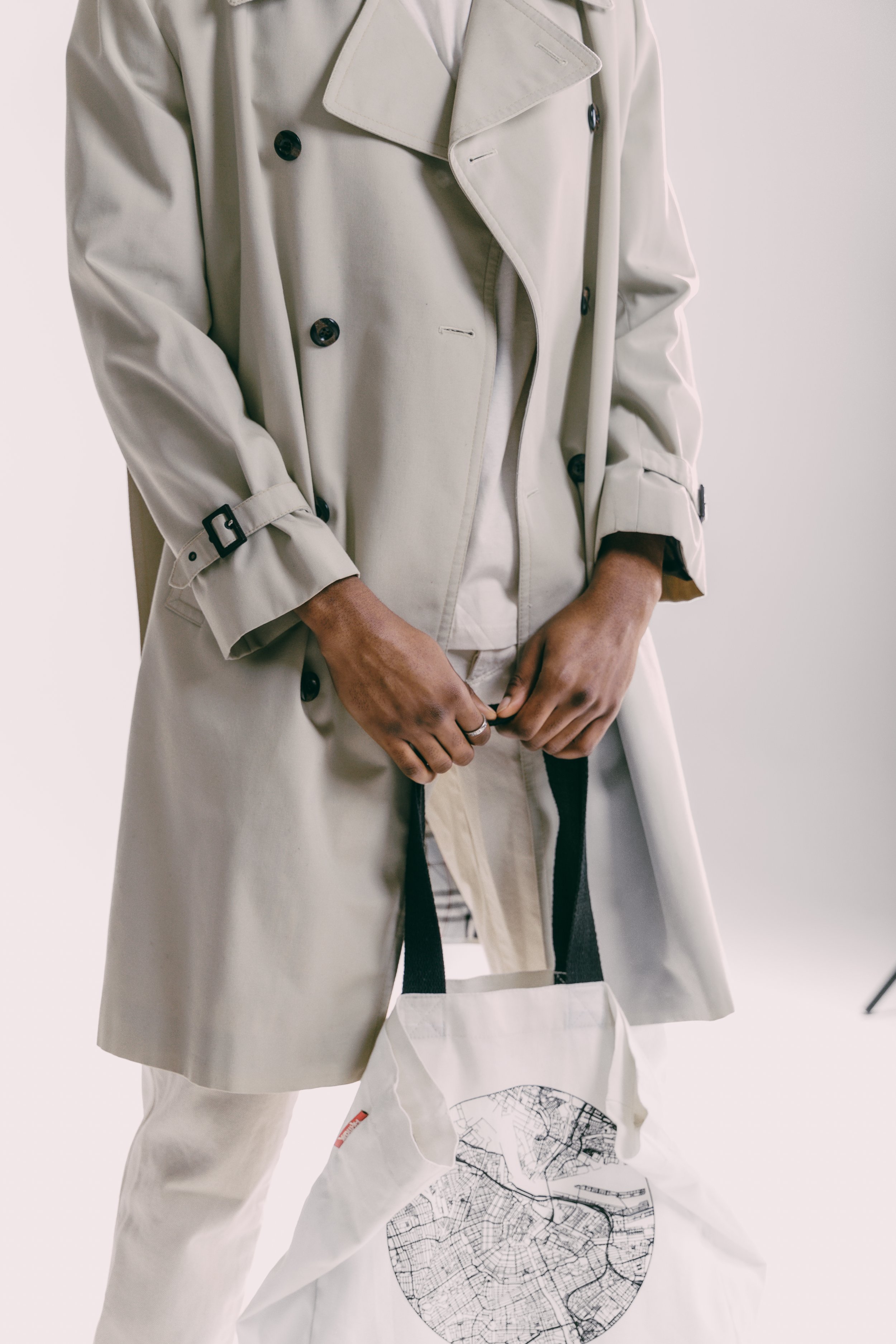 Person wearing a beige trench coat and holding a white tote bag with a city map design.