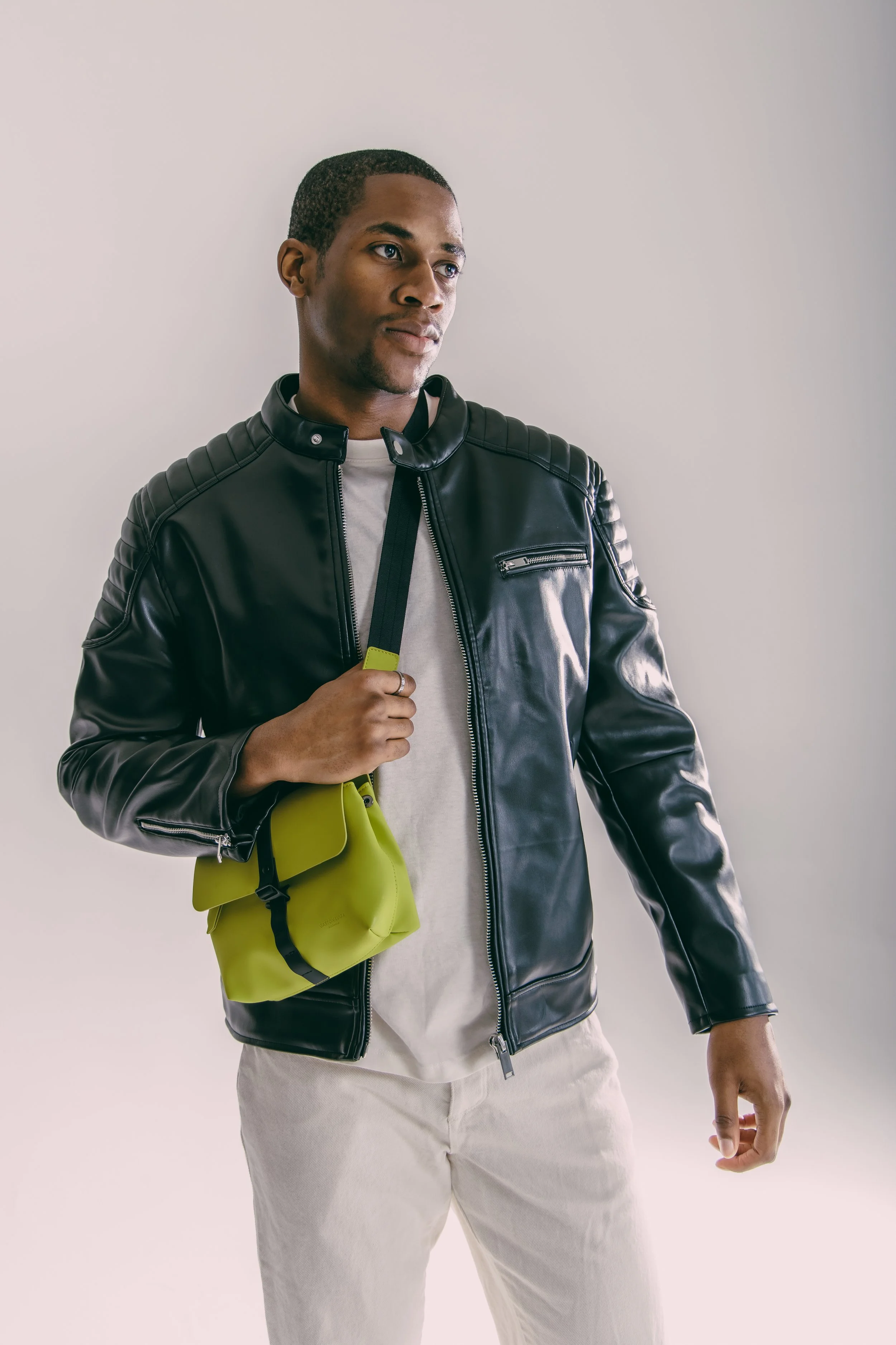 A young man wearing a black leather jacket and holding a small lime green bag with a black strap.