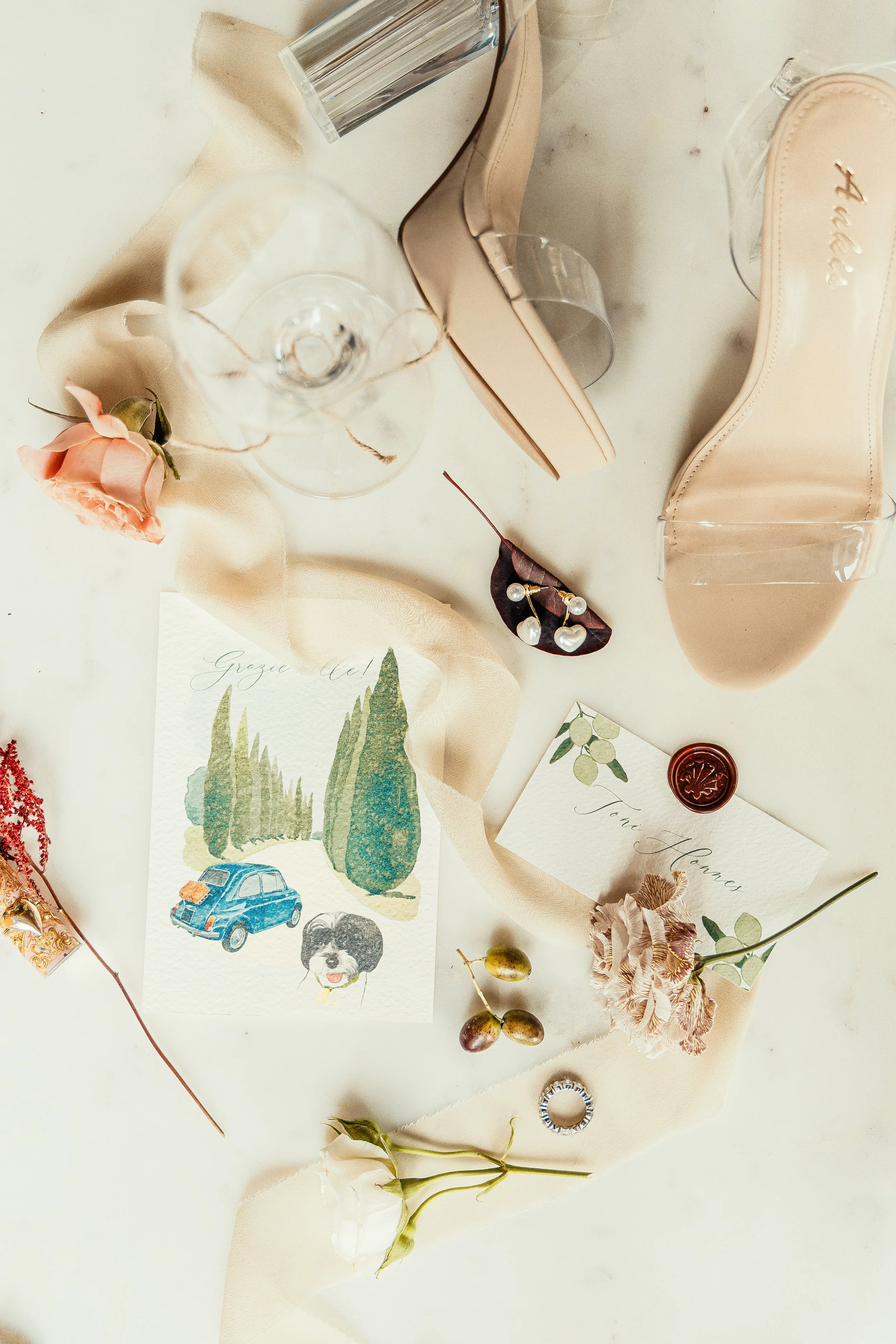 An assortment of items including a watercolor illustration, jewelry, flowers, and stationery on a white surface.