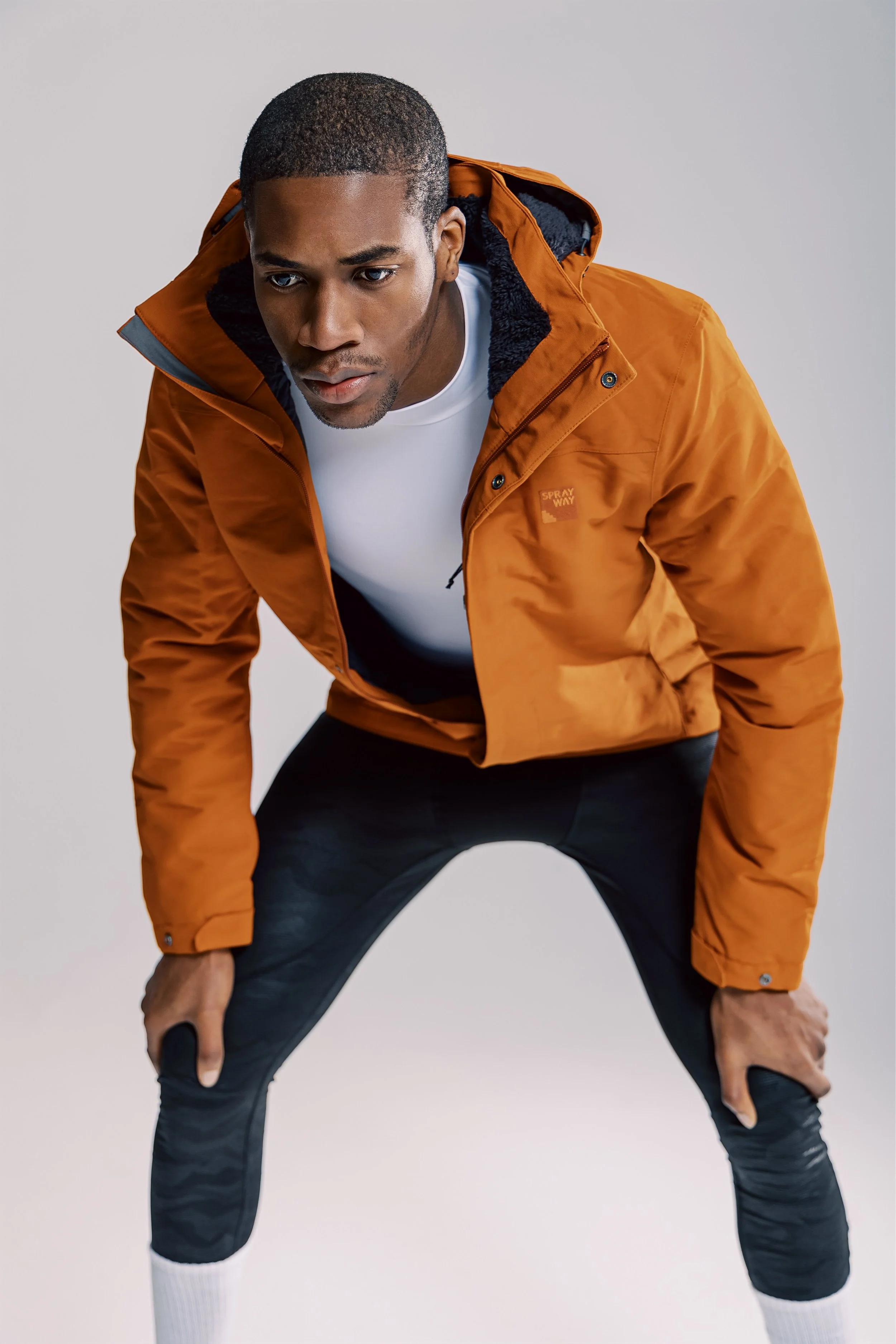 Man in orange jacket and black sportswear in a crouching stance.