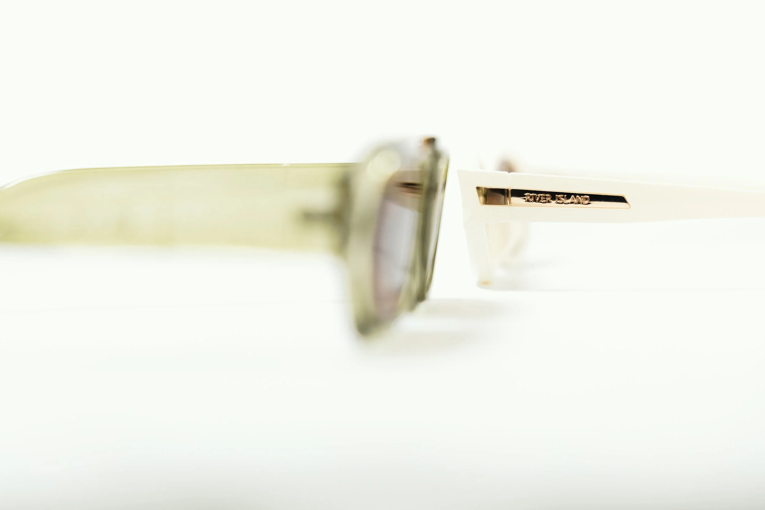 Close-up of sunglasses with 'River Island' on the white arm, on a white surface.
