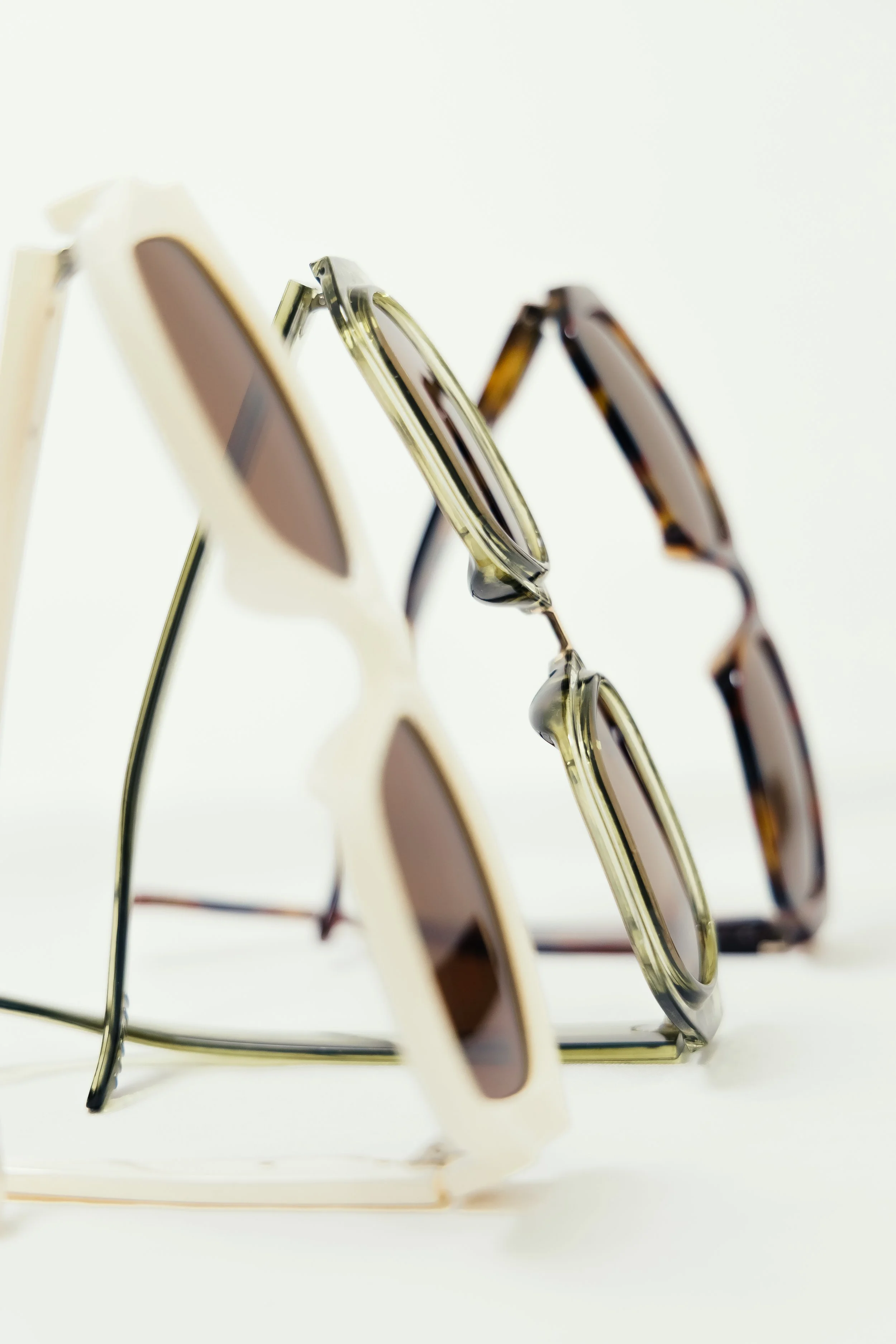 Three pairs of sunglasses on a white surface, arranged in a vertical line.