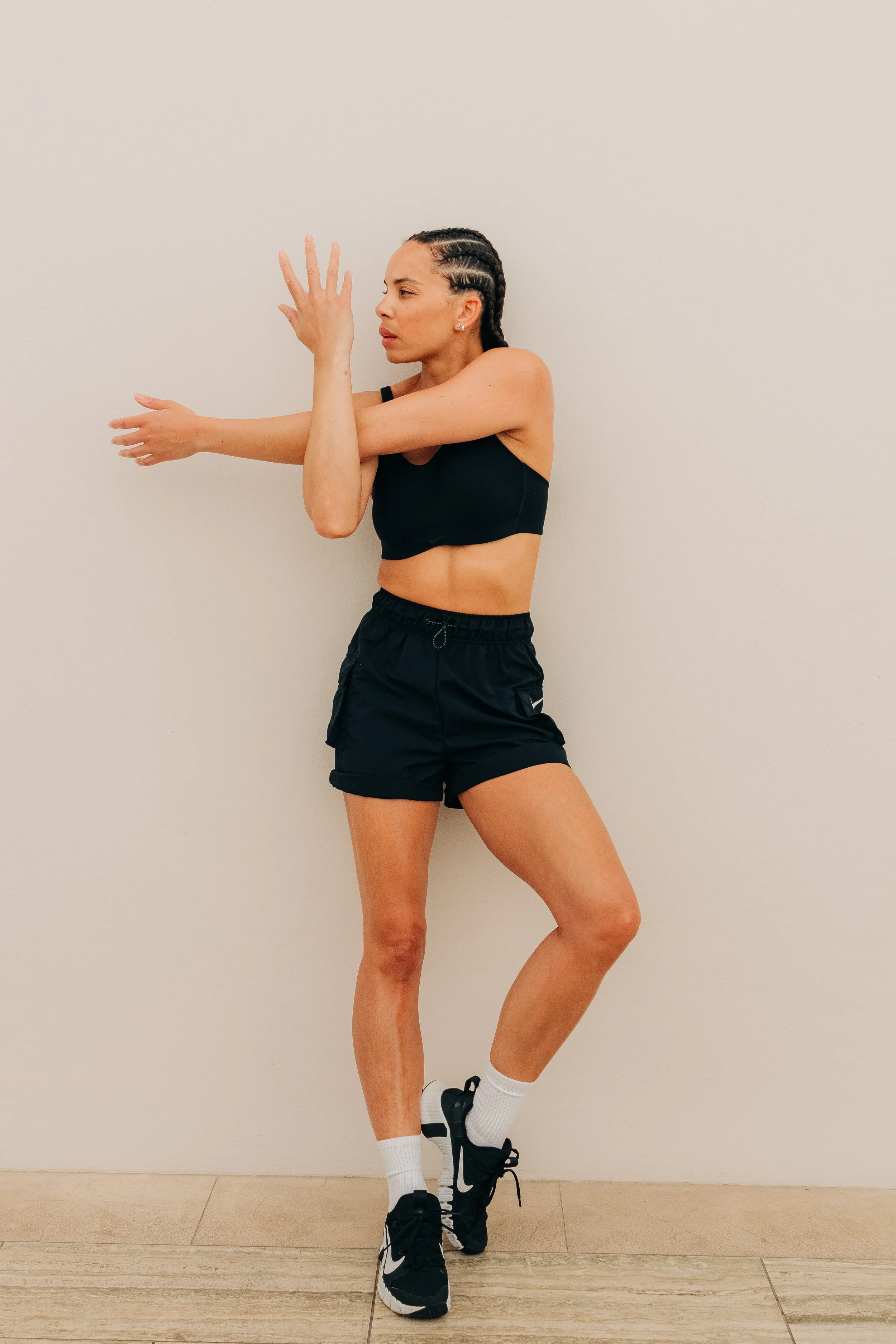Athletic woman performing a stretching exercise against a plain wall.