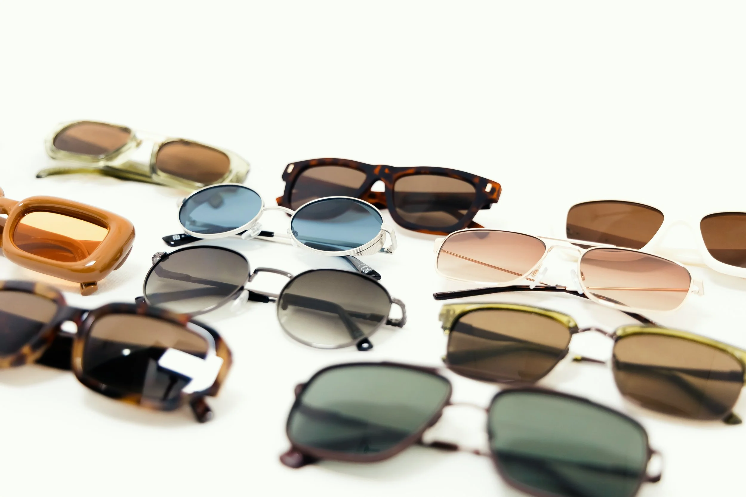 Multiple pairs of sunglasses in various styles and colors arranged on a white background.