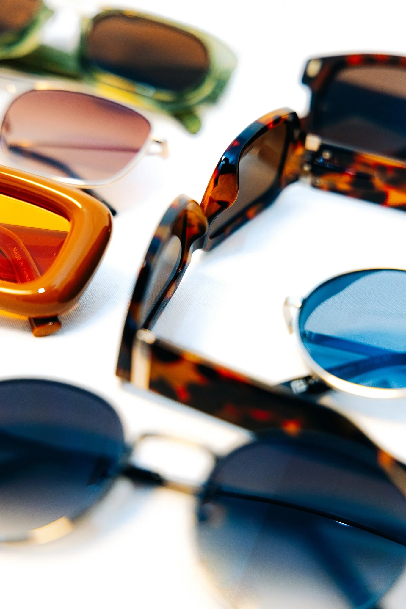 Multiple pairs of sunglasses with different colored lenses and frames on a white surface.