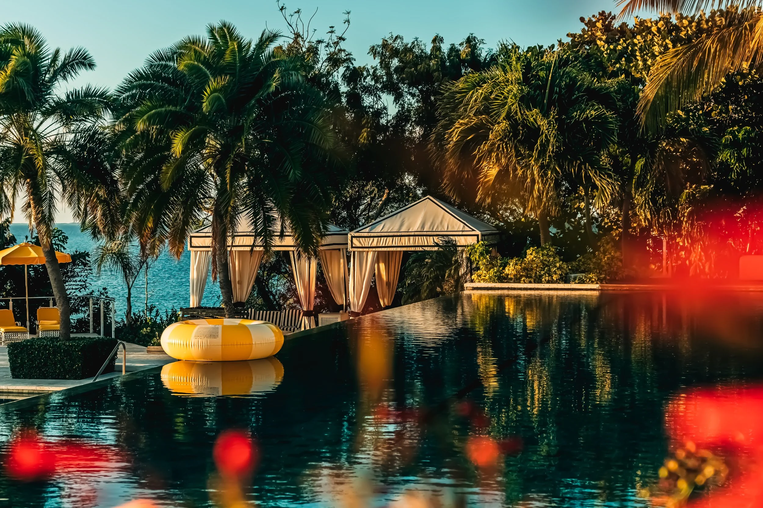 Palm trees and cabanas are visible near a swimming pool during sunset.