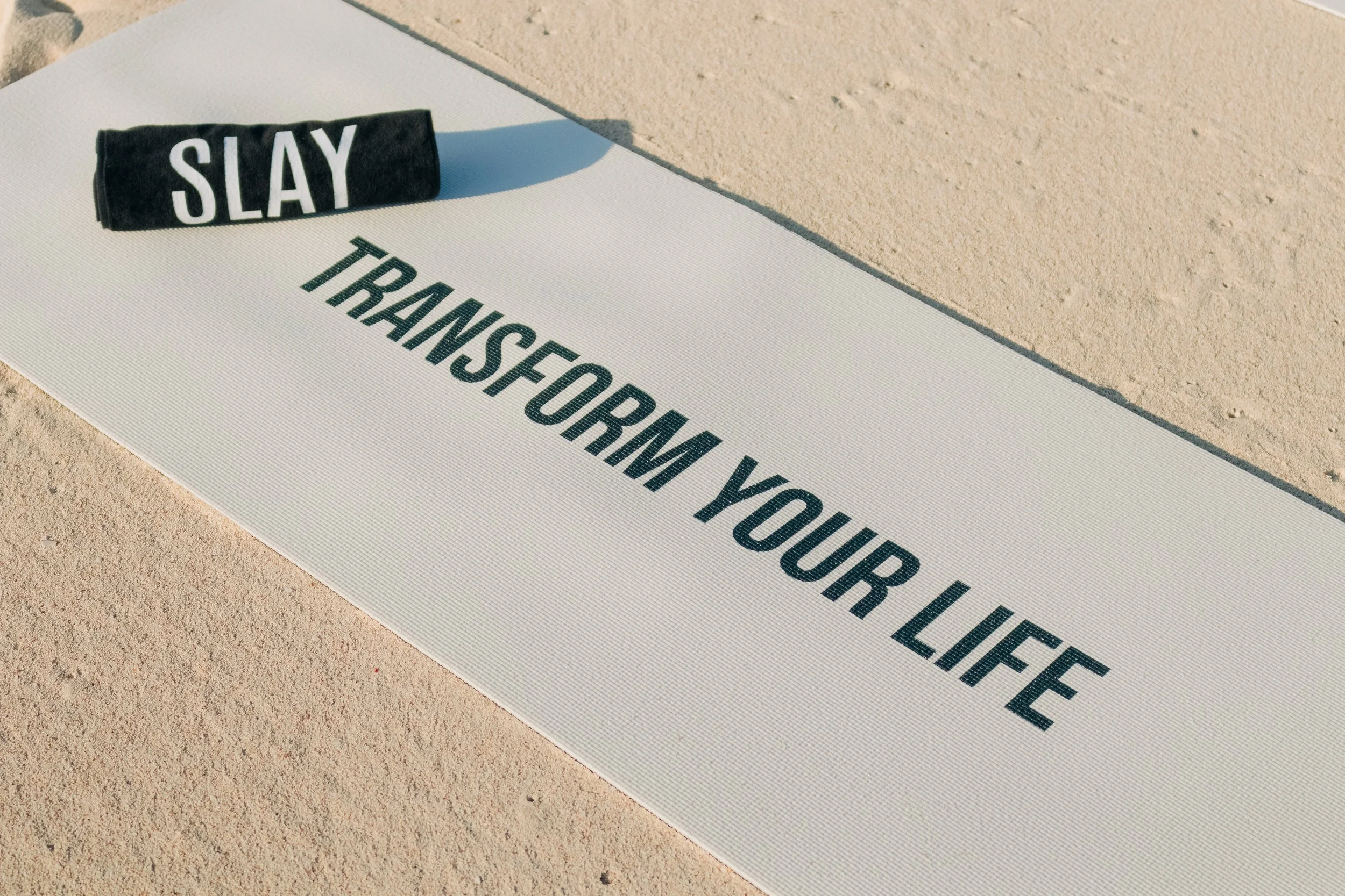 Yoga mat outdoors on sandy ground with a black headband labeled 'SLAY'.